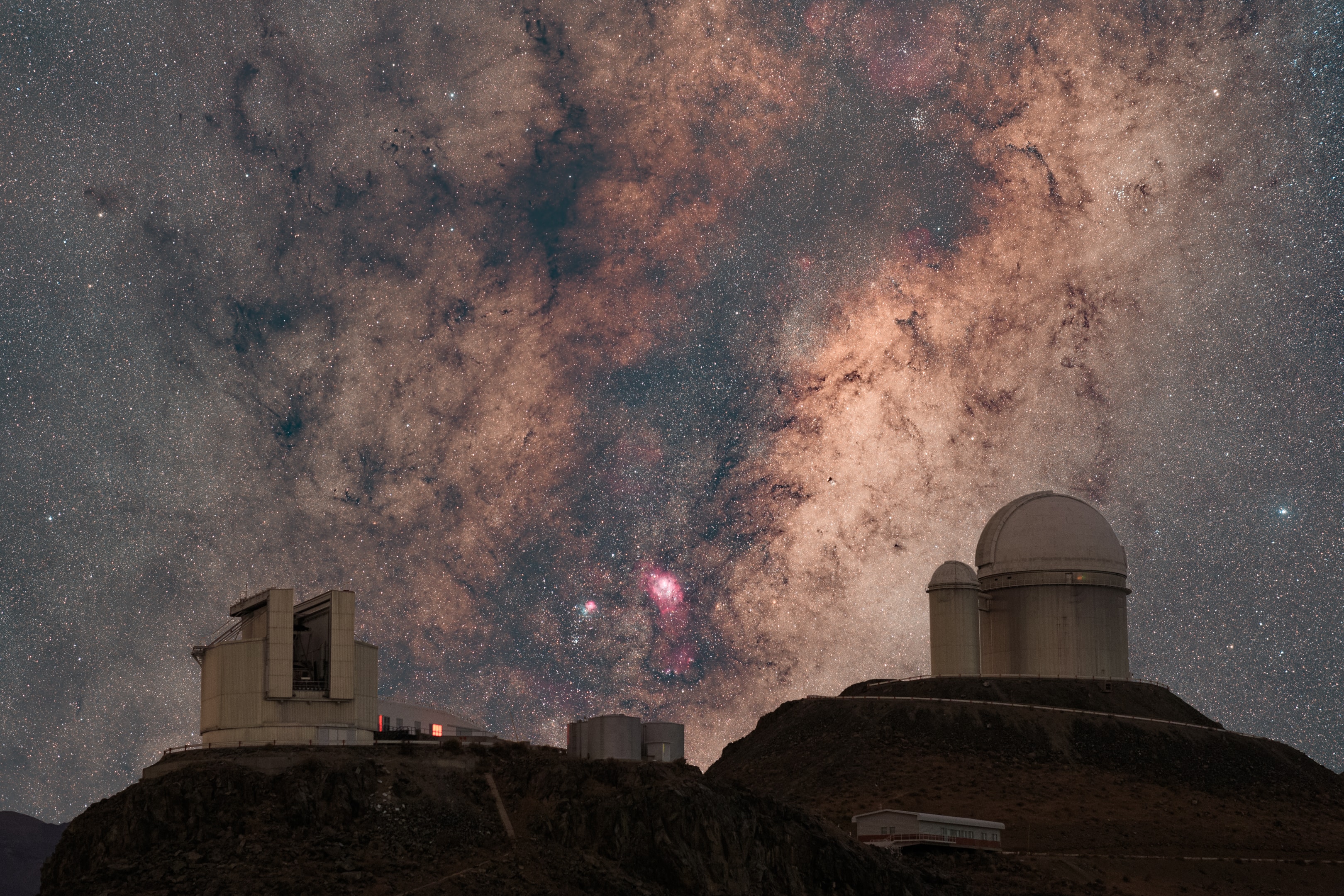 The core of the Milky Way is rising beyond the Chilean mountain-top La Silla Observatory in this deep night skyscape. Seen toward the constellation Sagittarius, our home galaxy's center is flanked on the left, by the European Southern Observatory's New Technology Telescope which pioneered the use of active optics to accurately control the shape of large telescope mirrors. To the right stands the ESO 3.6-meter Telescope, home of the exoplanet hunting HARPS and NIRPS spectrographs. Between them, the galaxy's central bulge is filled with obscuring clouds of interstellar dust, bright stars, clusters, and nebulae. Prominent reddish hydrogen emission from the star-forming Lagoon Nebula, M8, is near center. The Trifid Nebula, M20, combines blue light of a dusty reflection nebula with reddish emission just left of the cosmic Lagoon. Both are popular stops on telescopic tours of the galactic center. The composited image is a stack of separate exposures for ground and sky made in April 2023, all captured consecutively with the same framing and camera equipment.