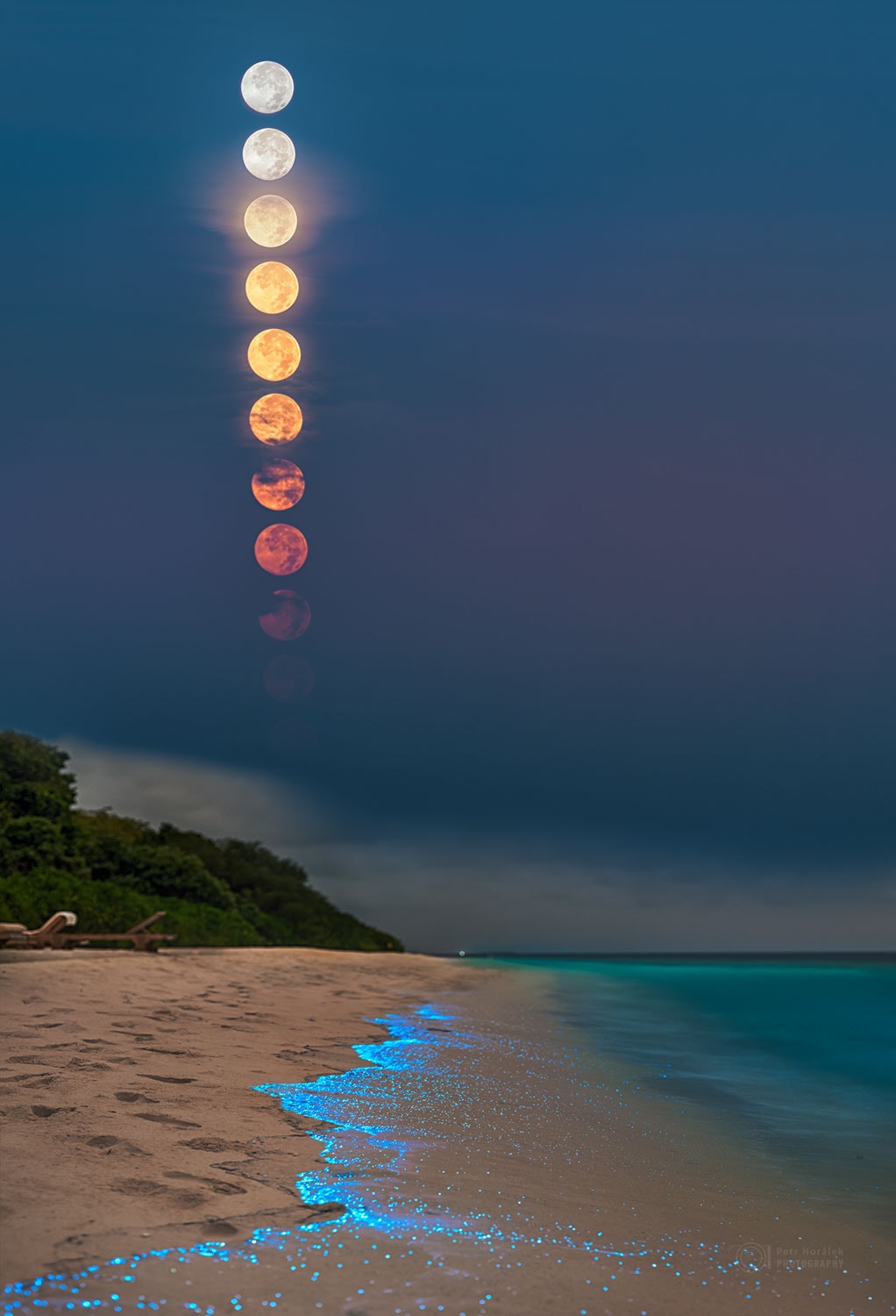 What glows in the night? This night featured a combination of usual and unusual glows. Perhaps the most usual glow was from the Moon, a potentially familiar object. The full Moon's nearly vertical descent results from the observer being near Earth's equator. As the Moon sets, air and aerosols in Earth's atmosphere preferentially scatter out blue light, making the Sun-reflecting satellite appear reddish when near the horizon.                                                                        Perhaps the most unusual glow was from the bioluminescent plankton, likely less familiar objects. These microscopic creatures glow blue, it is thought, primarily to surprise and deter predators. In this case, the glow was caused primarily by plankton-containing waves crashing onto the beach. The image was taken on Soneva Fushi Island, Maldives just over one year ago.   Your Sky Surprise: What picture did APOD feature on your birthday? (post 1995)