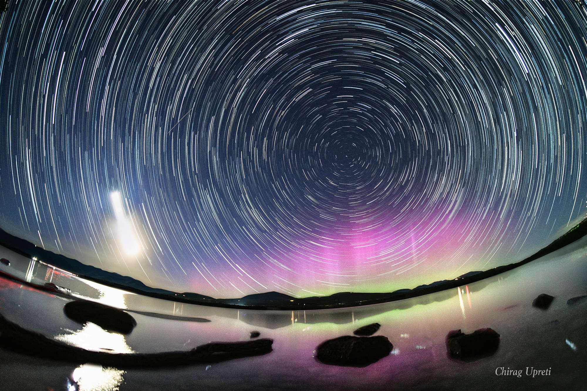 Graceful star trail arcs reflect planet Earth's daily rotation in this colorful night skyscape. To create the timelapse composite, on May 12 consecutive exposures were recorded with a camera fixed to a tripod on the shores of the Ashokan Reservoir, in the Catskills region of New York, USA. North star Polaris is near the center of the star trail arcs. The broad trail of a waxing crescent Moon is on the left, casting a strong reflection across the reservoir waters. With intense solar activity driving recent geomagnetic storms, the colorful aurora borealis or northern lights, rare to the region, shine under Polaris and the north celestial pole.   AuroraSaurus: Report your aurora observations