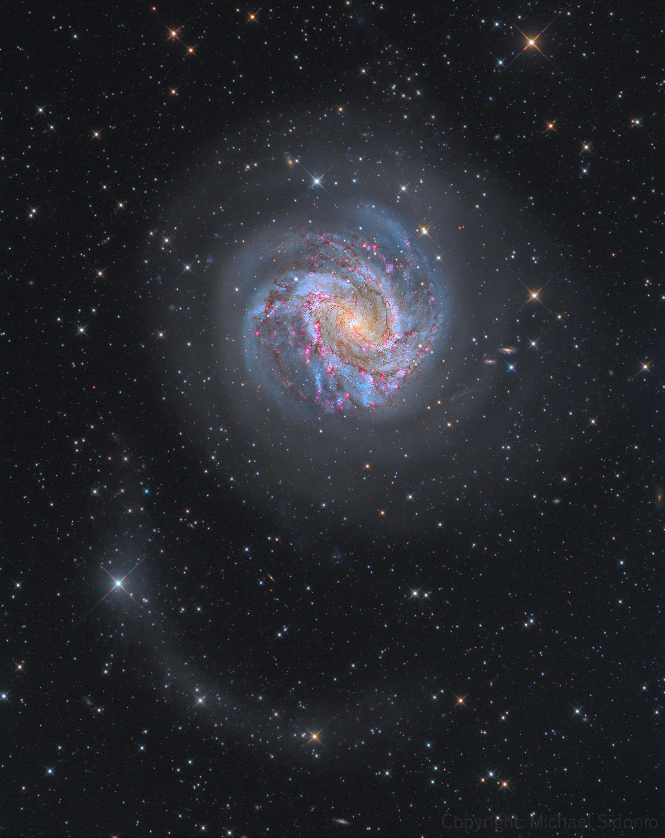 Big, bright, and beautiful, spiral galaxy M83 lies a mere twelve million light-years away, near the southeastern tip of the very long constellation Hydra. About 40,000 light-years across, M83 is known as the Southern Pinwheel for its pronounced spiral arms. But the wealth of reddish star forming regions found near the edges of the arms' thick dust lanes, also suggest another popular moniker for M83, the Thousand-Ruby Galaxy. This new deep telescopic digital image also records the bright galaxy's faint, extended halo. Arcing toward the bottom of the cosmic frame lies a stellar tidal stream, debris drawn from massive M83 by the gravitational disruption of a smaller, merging satellite galaxy. Astronomers David Malin and Brian Hadley found the elusive star stream in the mid 1990s by enhancing photographic plates.