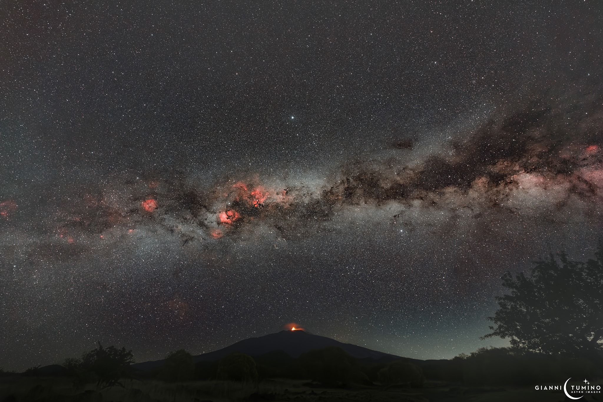 A glow from the summit of Mount Etna, famous active stratovolcano of planet Earth, stands out along the horizon in this mountain and night skyscape. Bands of diffuse light from congeries of innumerable stars along the Milky Way galaxy stretch across the sky above. In silhouette, the Milky Way's massive dust clouds are clumped along the galactic plane. Also familiar to northern skygazers are bright stars Deneb, Vega, and Altair, the Summer Triangle straddling dark nebulae and luminous star clouds poised over the volcanic peak. The deep combined exposures reveal the light of active star forming regions along the Milky Way, echoing Etna's ruddy hue in the northern hemisphere summer's night.