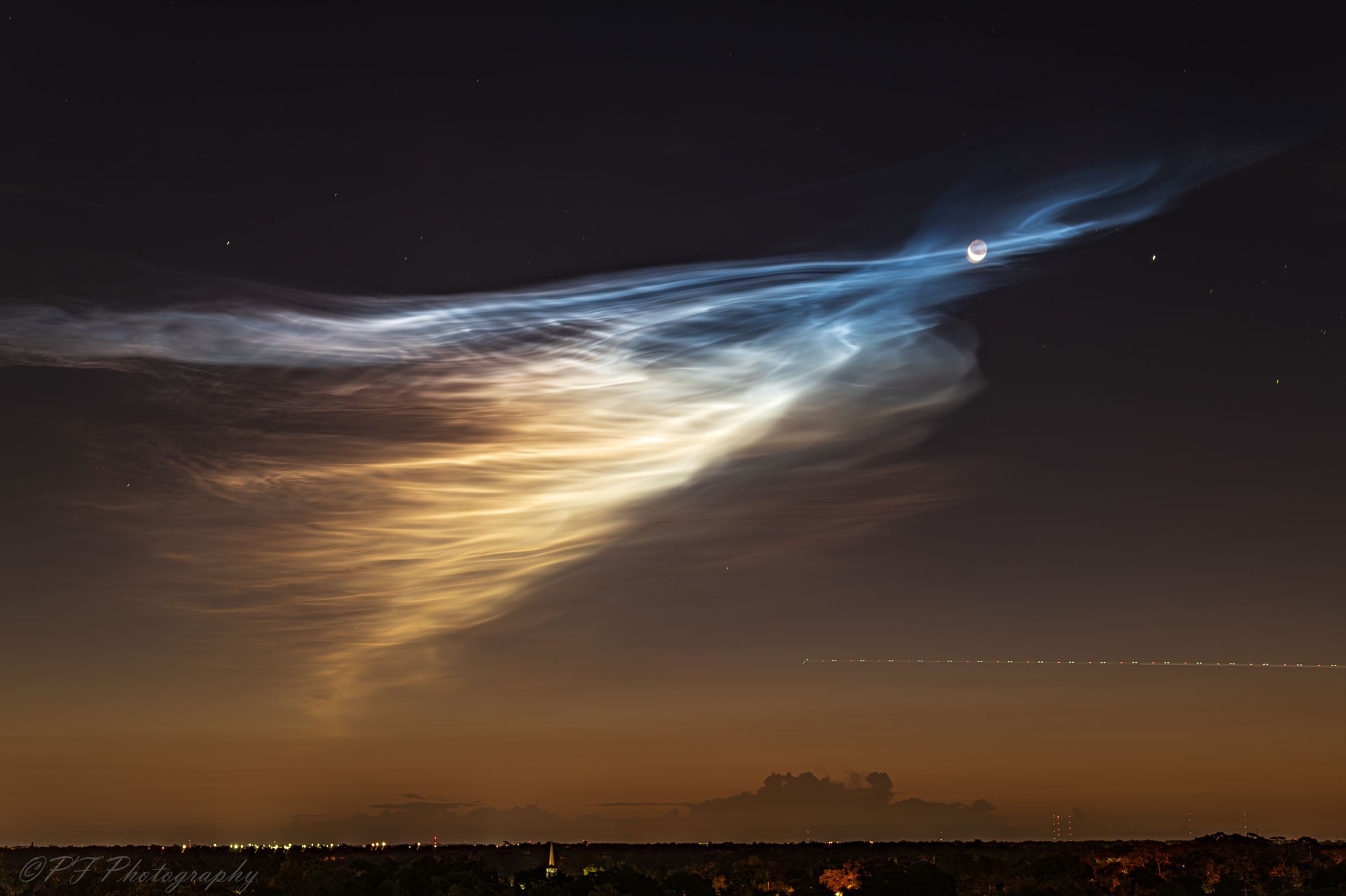 These clouds are doubly unusual. First, they are rare noctilucent clouds, meaning that they are visible at night -- but only just before sunrise or just after sunset.  Second, the source of these noctilucent clouds is actually known. In this rare case, the source of the sunlight-reflecting ice-crystals in the upper atmosphere can be traced back to the launch of a nearby SpaceX rocket about 30 minutes earlier.  Known more formally as polar mesospheric clouds, the vertex of these icy wisps happens to converge just in front of a rising crescent Moon. The featured image -- and accompanying video -- were captured over Orlando, Florida, USA about a week ago.  The bright spot to the right of the Moon is the planet Jupiter, while the dotted lights above the horizon on the right are from an airplane.