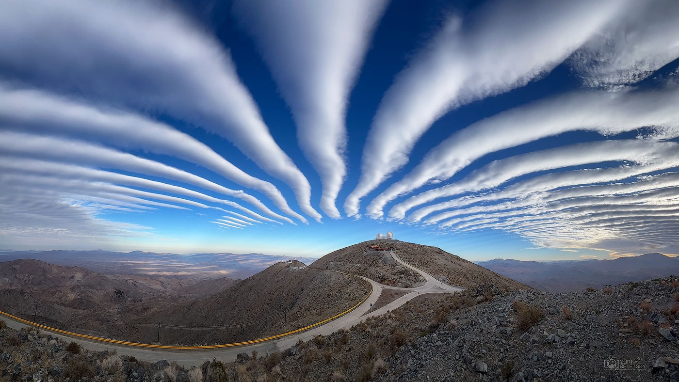 What's happening with these clouds?  While it may seem that these long and thin clouds are pointing toward the top of a hill, and that maybe a world-famous observatory is located there, only part of that is true. In terms of clouds, the formation is a chance superposition of impressively periodic undulating air currents in Earth's lower atmosphere. Undulatus, a type of Asperitas cloud, form at the peaks where the air is cool enough to cause the condensation of opaque water droplets.  The wide-angle nature of the panorama creates the illusion that the clouds converge over the hill.  In terms of land, there really is a world-famous observatory at the top of that peak: the Carnegie Science's Las Campanas Observatory in the Atacama Desert of Chile.  The two telescope domes visible are the 6.5-meter Magellan Telescopes.  The featured coincidental vista was a surprise but was captured by the phone of a quick-thinking photographer in late September.   Your Sky Surprise: What picture did APOD feature on your birthday? (post 1995)