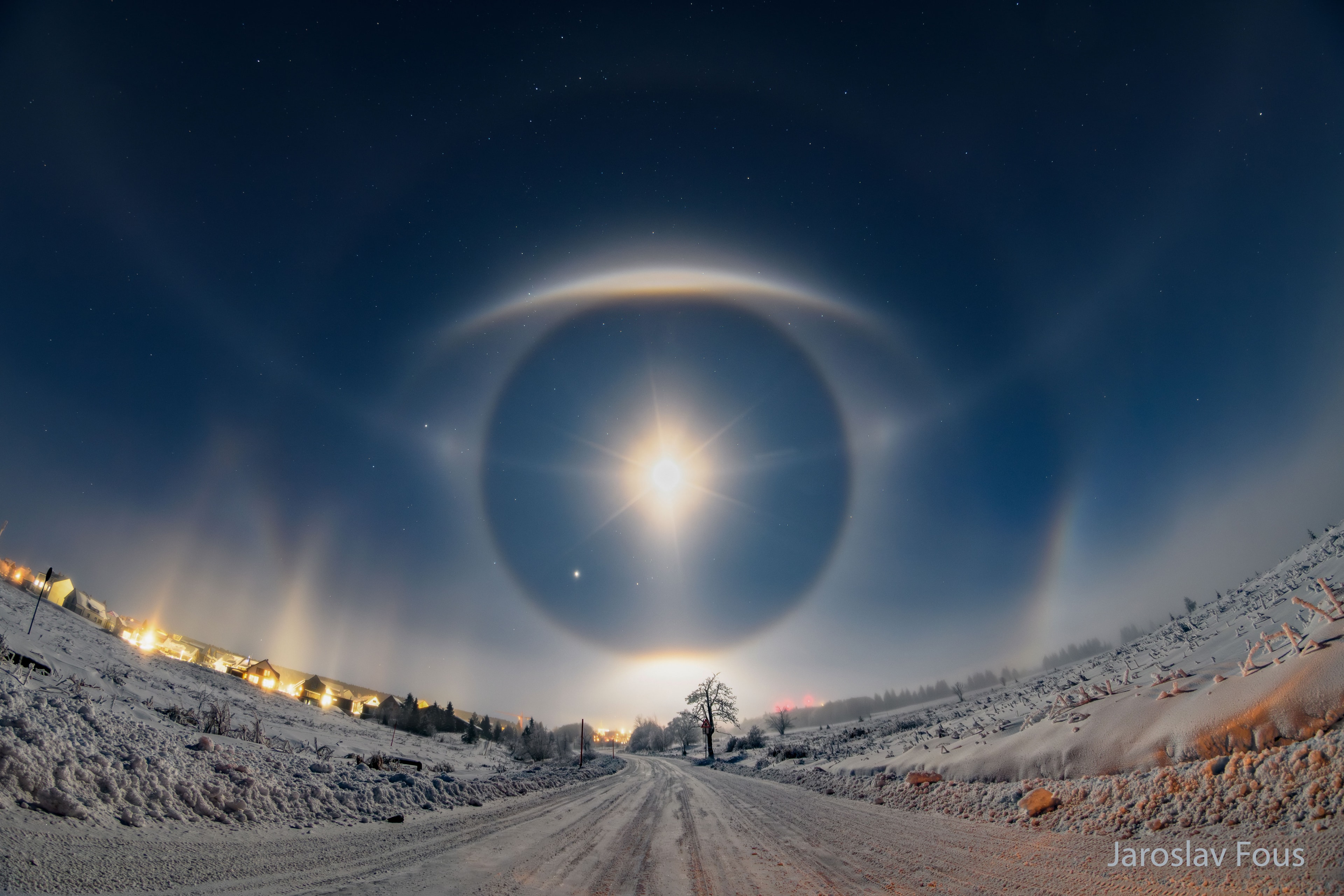 Why is there a huge eye in the sky? Diamond dust. That is an informal term for small ice crystals that form in the air and flitter to the ground. Because these crystals are geometrically shaped, they can together reflect light from the Sun or Moon to your eyes in a systematic way, causing huge halos and unusual arcs to appear. And sometimes, together the result can seem like a giant eye looking right back at you. In the featured image taken in the Ore Mountains of the Czech Republic last week, a bright Moon rising through ice fog-filled air resulted in many of these magnificent sky illusions to be visible simultaneously.  Besides Moon dogs, tangent arcs, halos, and a parhelic circle, light pillars above distant lights are visible on the far left, while Jupiter and Mars can be found just inside the bottom of the 22-degree halo.    Your Sky Surprise: What picture did APOD feature on your birthday? (post 1995)