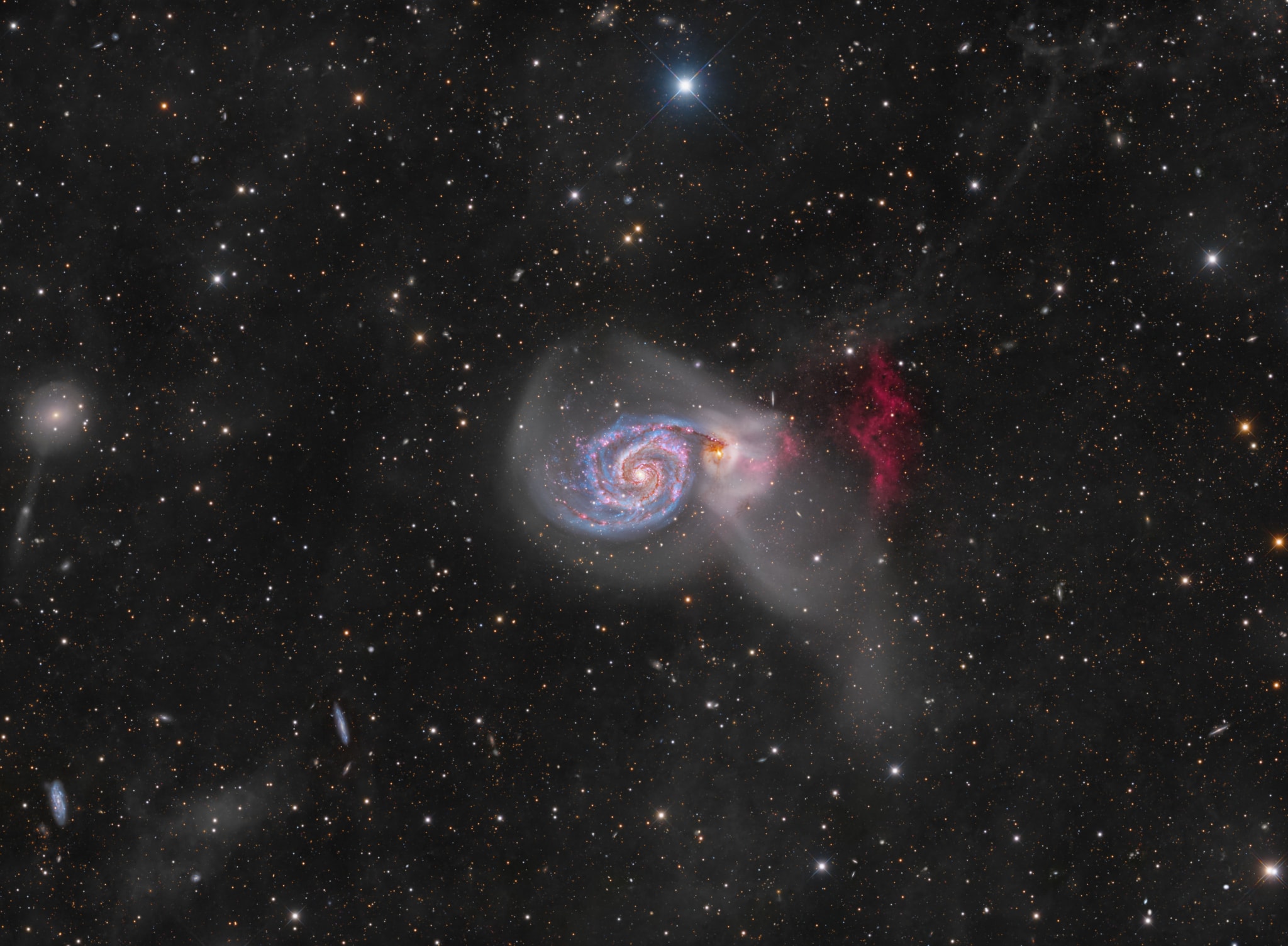 An intriguing pair of interacting galaxies, M51 is the 51st entry in Charles Messier's famous catalog. Perhaps the original spiral nebula, the large galaxy with whirlpool-like spiral structure seen nearly face-on is also cataloged as NGC 5194. Its spiral arms and dust lanes sweep in front of its smaller companion galaxy, NGC 5195. Some 31 million light-years distant, within the boundaries of the well-trained constellation Canes Venatici, M51 looks faint and fuzzy to the eye in direct telescopic views. But this remarkably deep image shows off stunning details of the galaxy pair's striking colors and fainter tidal streams. The image includes extensive narrowband data to highlight a vast reddish cloud of ionized hydrogen gas recently discovered in the M51 system and known to some as the H-alpha cliffs. Foreground dust clouds in the Milky Way and distant background galaxies are captured in the wide-field view. A continuing collaboration of astro-imagers using telescopes on planet Earth assembled over 3 weeks of exposure time to create this evolving portrait of M51.  Watch: The 2024 Geminid Meteor Shower