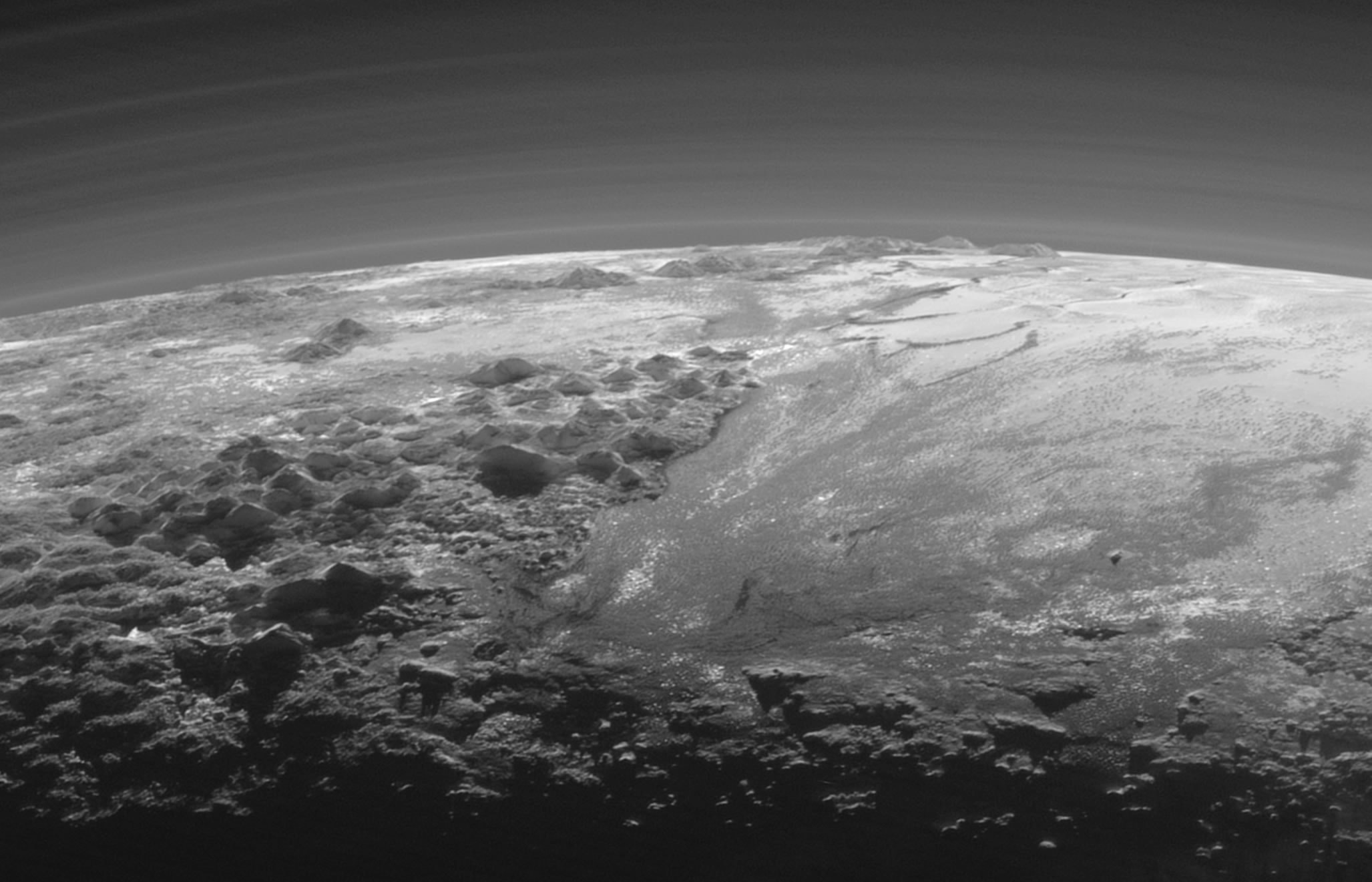 This shadowy landscape of majestic mountains and icy plains stretches toward the horizon on a small, distant world. It was captured from a range of about 18,000 kilometers when New Horizons looked back toward Pluto, 15 minutes after the spacecraft's closest approach on July 14, 2015. The dramatic, low-angle, near-twilight scene follows rugged mountains formally known as Norgay Montes from foreground left, and Hillary Montes along the horizon, giving way to smooth Sputnik Planum at right. Layers of Pluto's tenuous atmosphere are also revealed in the backlit view. With a strangely familiar appearance, the frigid terrain likely includes ices of nitrogen and carbon monoxide with water-ice mountains rising up to 3,500 meters (11,000 feet). That's comparable in height to the majestic mountains of planet Earth. The Plutonian landscape is 380 kilometers (230 miles) across.