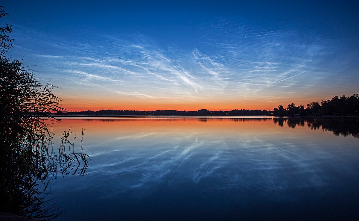 Transfusing sunlight as the sky grew darker, this exceptional display of noctilucent clouds was captured on July 10, reflected in the calm waters of Vallentuna Lake near Stockholm, Sweden. From the edge of space, about 80 kilometers above Earth's surface, the icy clouds themselves still reflect sunlight, even though the Sun is below the horizon as seen from the ground. Usually spotted at high latitudes in summer months, the night shining clouds have made a strong showing so far during the short northern summer nights. Also known as polar mesopheric clouds they are understood to form as water vapor driven into the cold upper atmosphere condenses on the fine dust particles supplied by disintegrating meteors or volcanic ash.