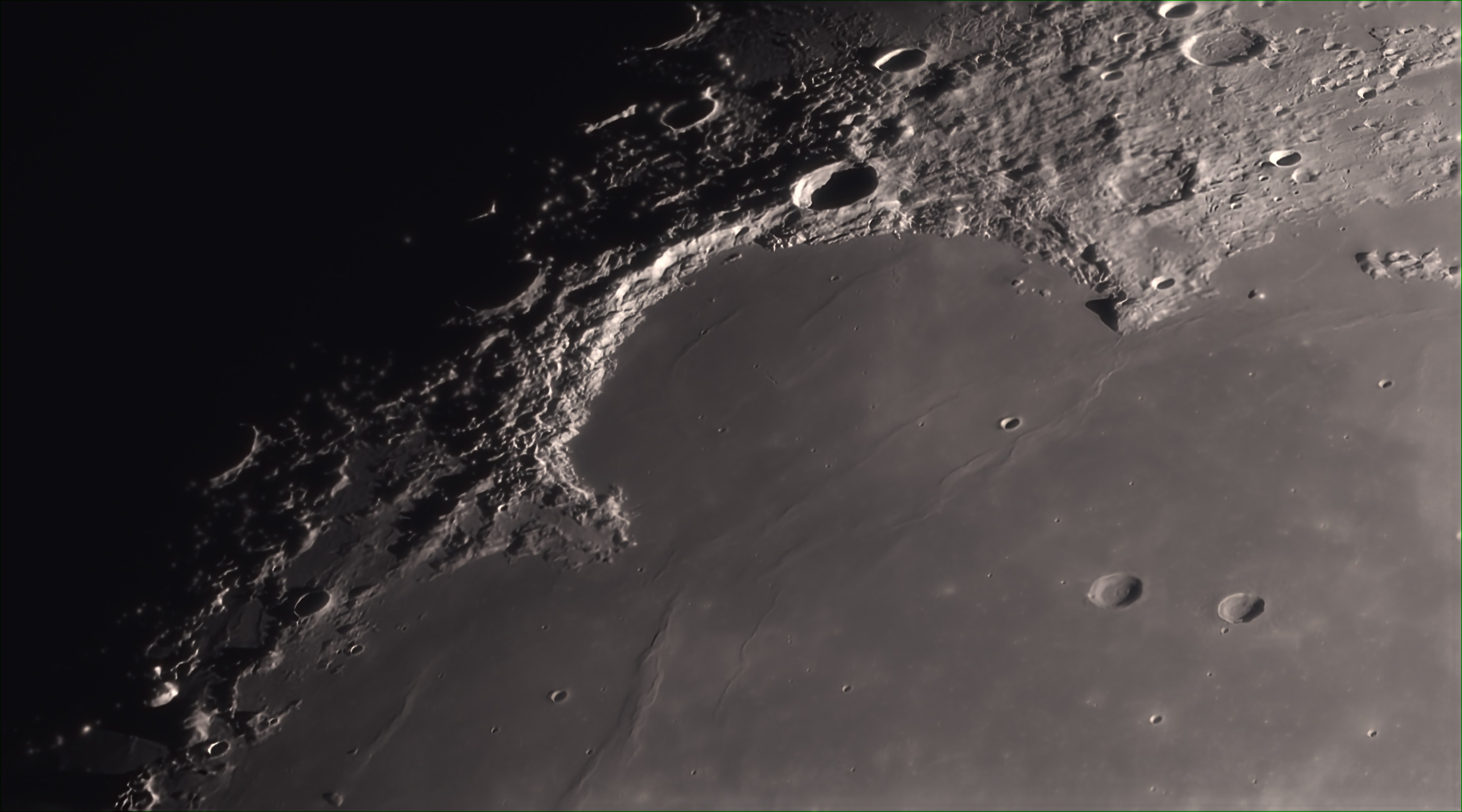 Dark, smooth regions that cover the Moon's familiar face are called by Latin names for oceans and seas. That naming convention is historical, though it may seem a little ironic to denizens of the space age who recognize the Moon as a mostly dry and airless world, and the smooth, dark areas as lava-flooded impact basins. For example, this telescopic lunar vista, looks over the expanse of the northwestern Mare Imbrium, or Sea of Rains and into the Sinus Iridum, the Bay of Rainbows. Ringed by the Jura Mountains (montes), the bay is about 250 kilometers across. Seen after local sunrise, the mountains form part of the Sinus Iridum impact crater wall. Their rugged sunlit arc is bounded at the top by Cape (promontorium) Laplace reaching nearly 3,000 meters above the bay's surface. At the bottom of the arc is Cape Heraclides, depicted by Giovanni Cassini in his 1679 telescope-based drawings mapping the moon as a moon maiden seen in profile with long, flowing hair.