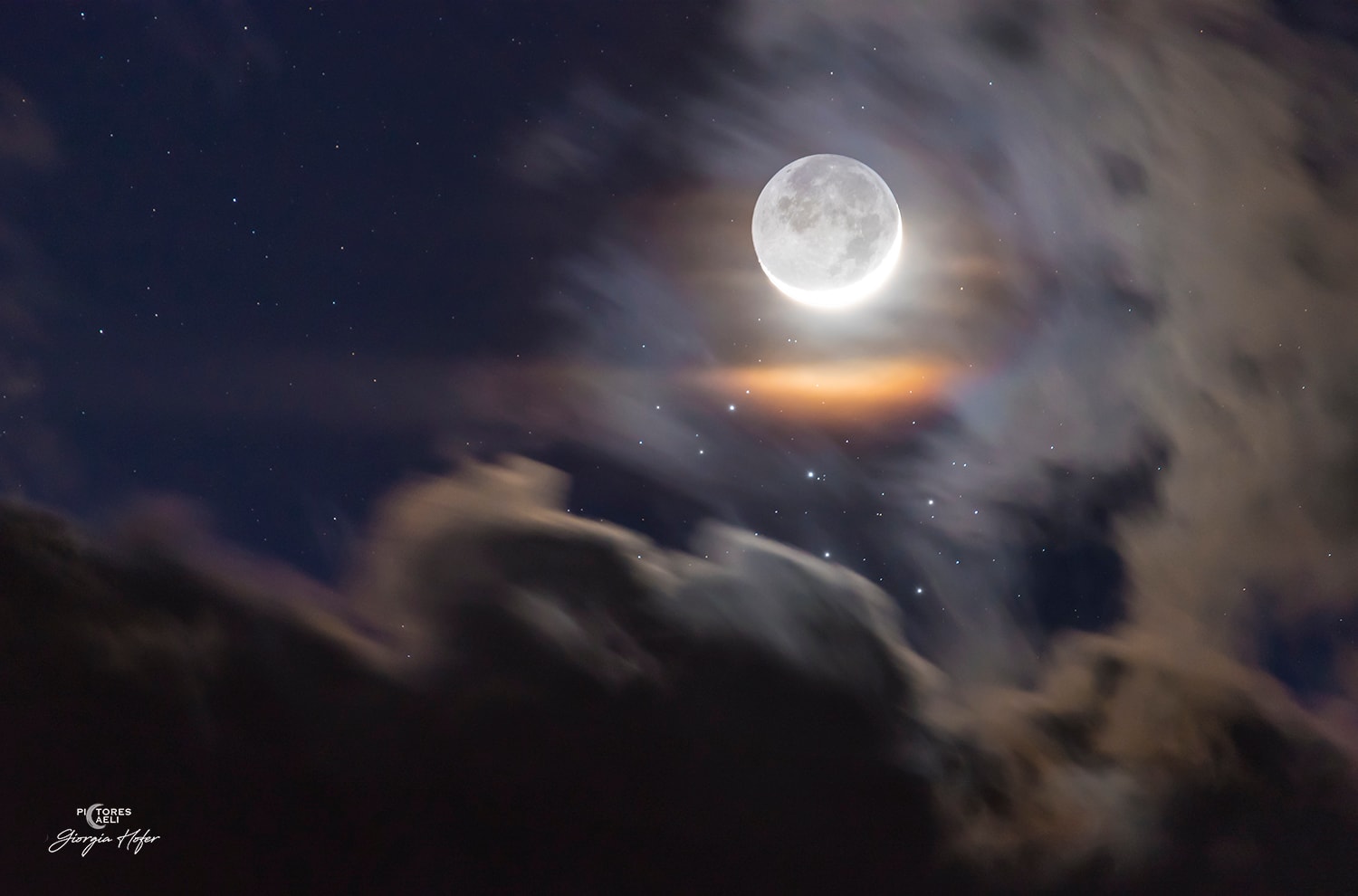 Sunlit arms of a crescent moon seem to embrace the faint lunar night side in this dramatic celestial scene from planet Earth. The single telephoto exposure tracking the sky was captured on the night of April 19, when a two day old Moon was near perigee in its elliptical orbit. On that date, the young Moon was also close on the sky to the lovely Pleiades Star Cluster. With the moonlight dimmed by clouds the Pleiades sister stars gather below the Moon's bright crescent, seen through a faint but colorful lunar corona. The lunar night side is illuminated by earthshine, sunlight reflected from the Earth itself. The Moon's ashen glow, also known as the "old moon in the young moon's arms", tends to be brighter in the northern hemisphere spring. And for now, the Moon's orbit takes it near the Pleiades stars each month in planet Earth's sky, though their close conjunctions are easiest to see when the Moon is near a crescent phase.