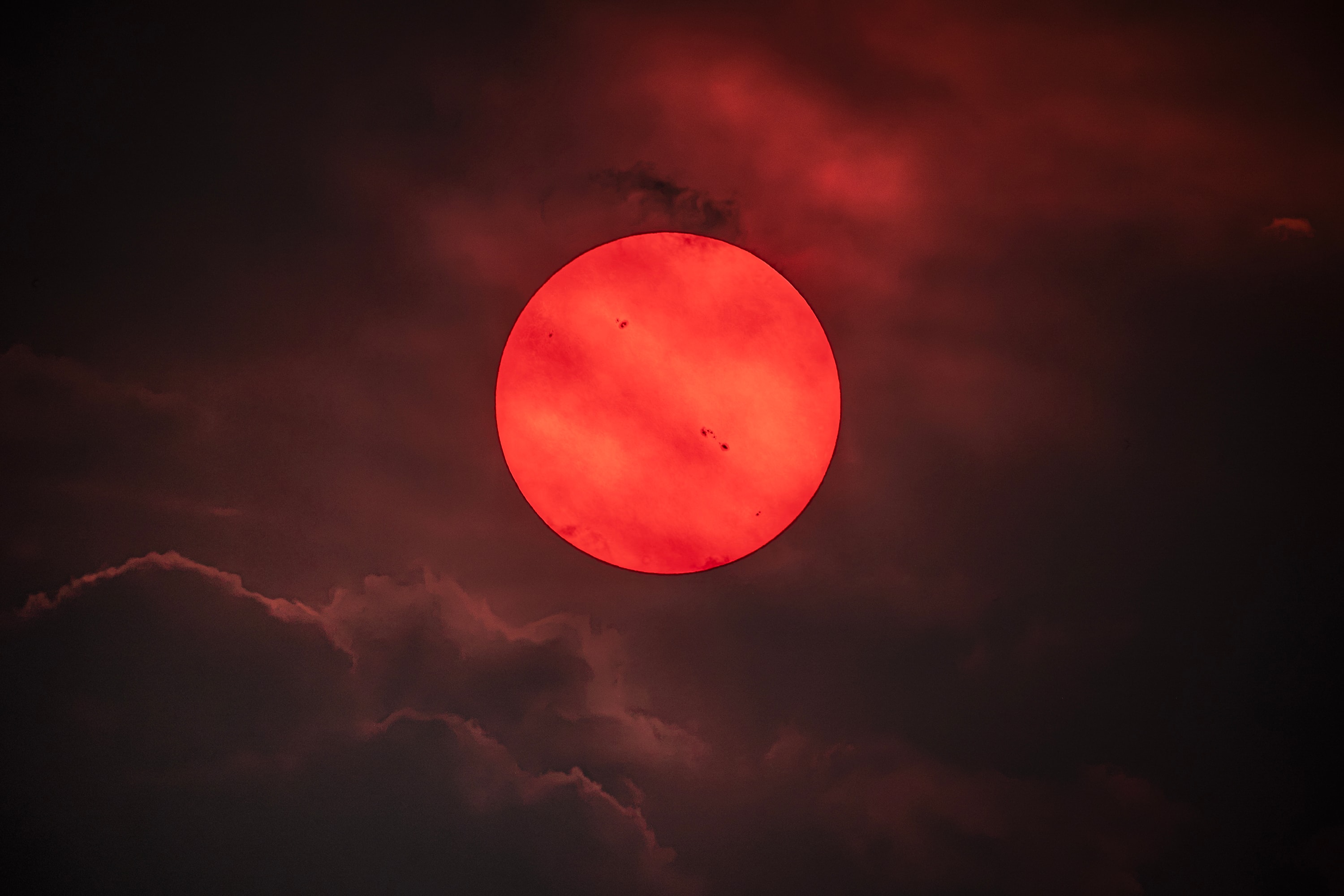 This could be the view from an exoplanet orbiting around a red dwarf star, but it is our own Sun.   This image was taken on July 22, 2026, in the Okanagan region in the Canadian province of British Columbia.   Wildfire smoke from the Pacific Northwest acted as a solar filter, allowing the photographer to take this photo of the Sun directly.   Several sunspots are also visible in this eerie image; just below and right of the center is AR 4493, a fast evolving, giant active solar region and sunspot group.     The smoke is made of tiny particles that help block and scatter light with bluer colors, so the light we see coming from the Sun is dimmer and redder than usual (but it is never safe to stare directly at the Sun).   Sunsets and sunrises are also more colorful because of the smoke.      Some 6 billion years from now, the Sun will actually start to turn redder as it approaches its red giant phase.