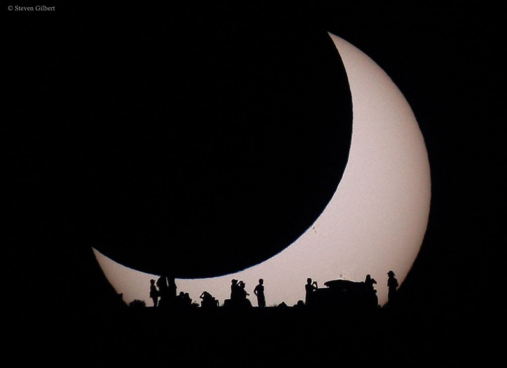 Have you contemplated your home star recently?  Featured here, a Sun partially eclipsed on the top left by the Moon is also seen eclipsed by earthlings contemplating the eclipse below.  This spectacular menagerie of silhouettes was taken in 2012 from the Glen Canyon National Recreation Area near Page, Arizona, USA, where park rangers and astronomers expounded on the unusual event to interested gatherers.  Also, faintly visible on the Sun's disk, just to the lower right of the dark Moon's disk, is a group of sunspots.  A new solar eclipse will occur this week and give many people in northern North America, Europe, and northwestern Africa a new chance to contemplate a partially eclipsed Sun. A thin swath of Earth from Greenland to Portugal will further experience a total solar eclipse. An open question is whether any meteors from the peaking Perseids will be visible during totality.