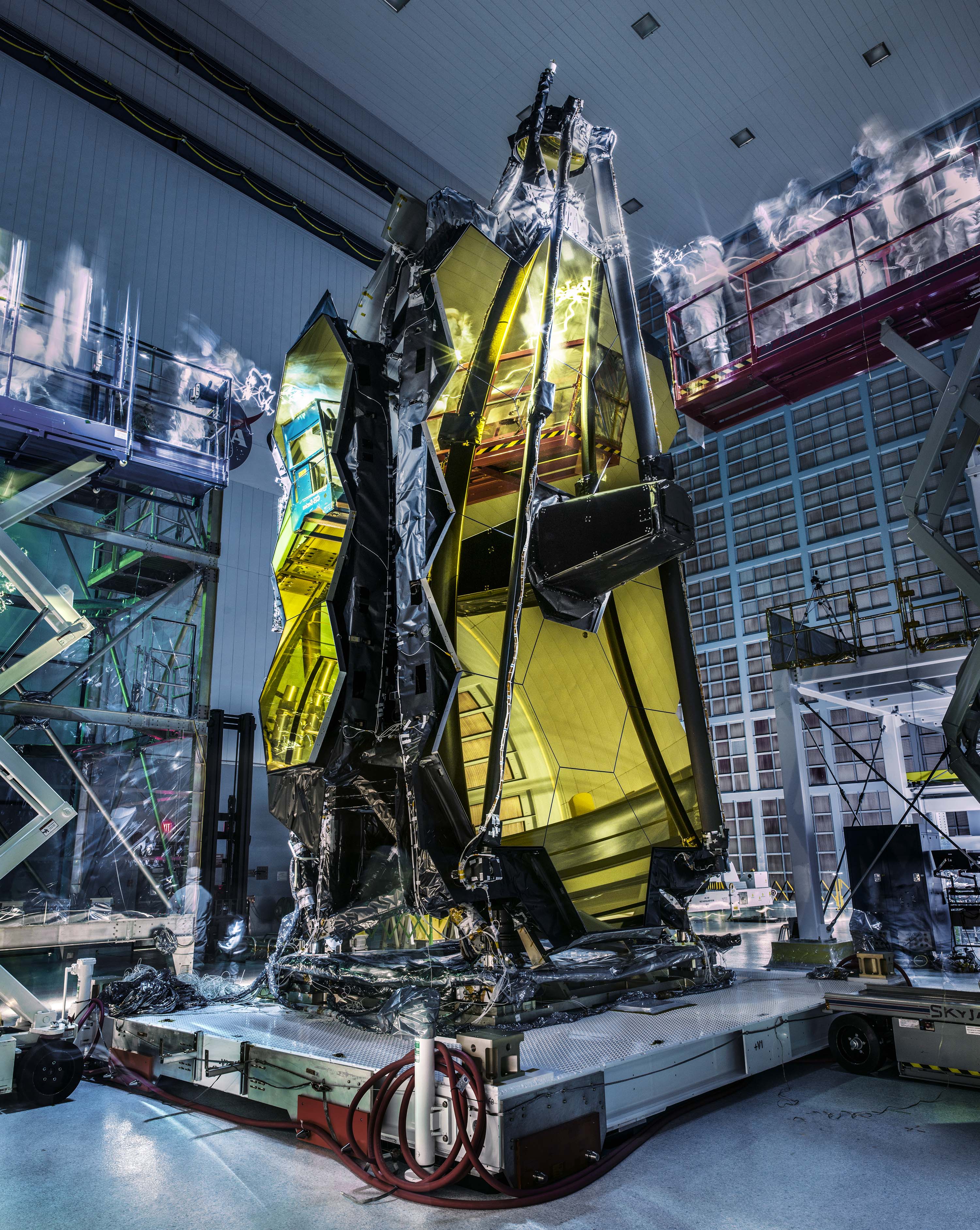 Ghosts aren't actually hovering over the James Webb Space Telescope. But the lights are out as it stands with gold tinted mirror segments and support structures folded in Goddard Space Flight Center's Spacecraft Systems Development and Integration Facility clean room. Following vibration and acoustic testing, bright flashlights and ultraviolet lights are played over the stationary telescope looking for contamination, easier to spot in a darkened room. In the dimness the camera's long exposure creates the ghostly apparitions, blurring the moving lights and engineers. A scientific successor to Hubble, the James Webb Space Telescope is optimized for the infrared exploration of the early Universe. Its planned launch is in 2018 from French Guiana on a European Space Agency Ariane 5 rocket.