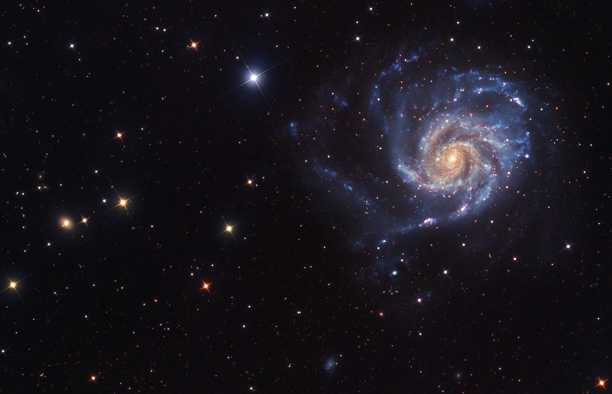 Big, beautiful spiral galaxy M101 is one of the last entries in Charles Messier's famous catalog, but definitely not one of the least. About 170,000 light-years across, this galaxy is enormous, almost twice the size of our own Milky Way galaxy. M101 was also one of the original spiral nebulae observed by Lord Rosse's large 19th century telescope, the Leviathan of Parsontown. M101 shares this modern telescopic field of view with spiky foreground stars within the Milky Way, and more distant background galaxies. The colors of the Milky Way stars can also be found in the starlight from the large island universe. Its core is dominated by light from cool yellowish stars. Along its grand spiral arms are the blue colors of hotter, young stars mixed with obscuring dust lanes and pinkish star forming regions. Also known as the Pinwheel Galaxy, M101 lies within the boundaries of the northern constellation Ursa Major, about 25 million light-years away.