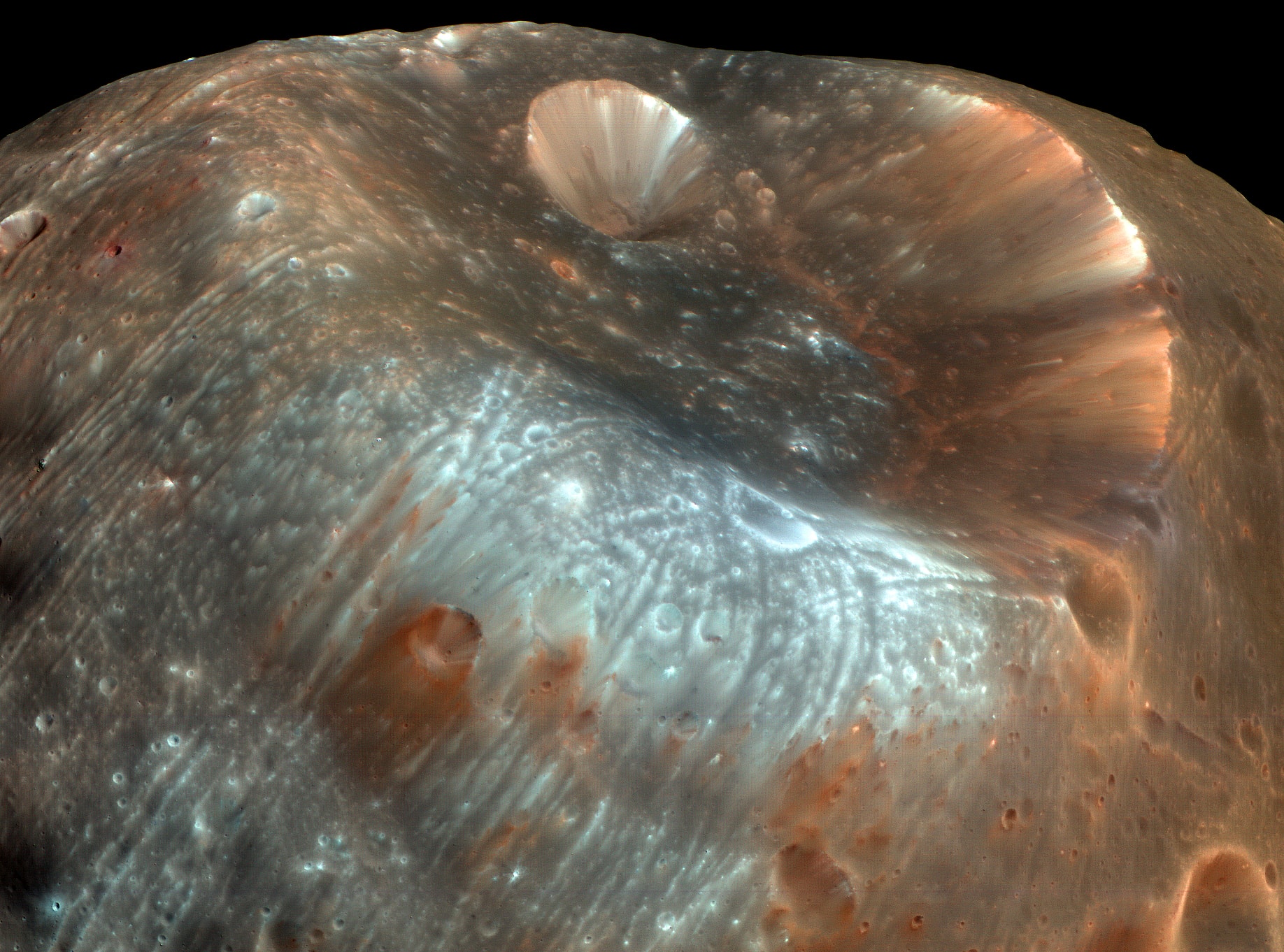 Stickney Crater, the largest crater on the martian moon Phobos, is named for Chloe Angeline Stickney Hall, mathematician and wife of astronomer Asaph Hall. Asaph Hall discovered both the Red Planet's moons in 1877. Over 9 kilometers across, Stickney is nearly half the diameter of Phobos itself, so large that the impact that blasted out the crater likely came close to shattering the tiny moon. This stunning, enhanced-color image of Stickney and surroundings was recorded by the HiRISE camera onboard the Mars Reconnaissance Orbiter as it passed within some six thousand kilometers of Phobos in March of 2008. Even though the surface gravity of asteroid-like Phobos is less than 1/1000th Earth's gravity, streaks suggest loose material slid down inside the crater walls over time. Light bluish regions near the crater's rim could indicate a relatively freshly exposed surface. The origin of the curious grooves along the surface is mysterious but may be related to the crater-forming impact. Follow: Mars InSight Launch
