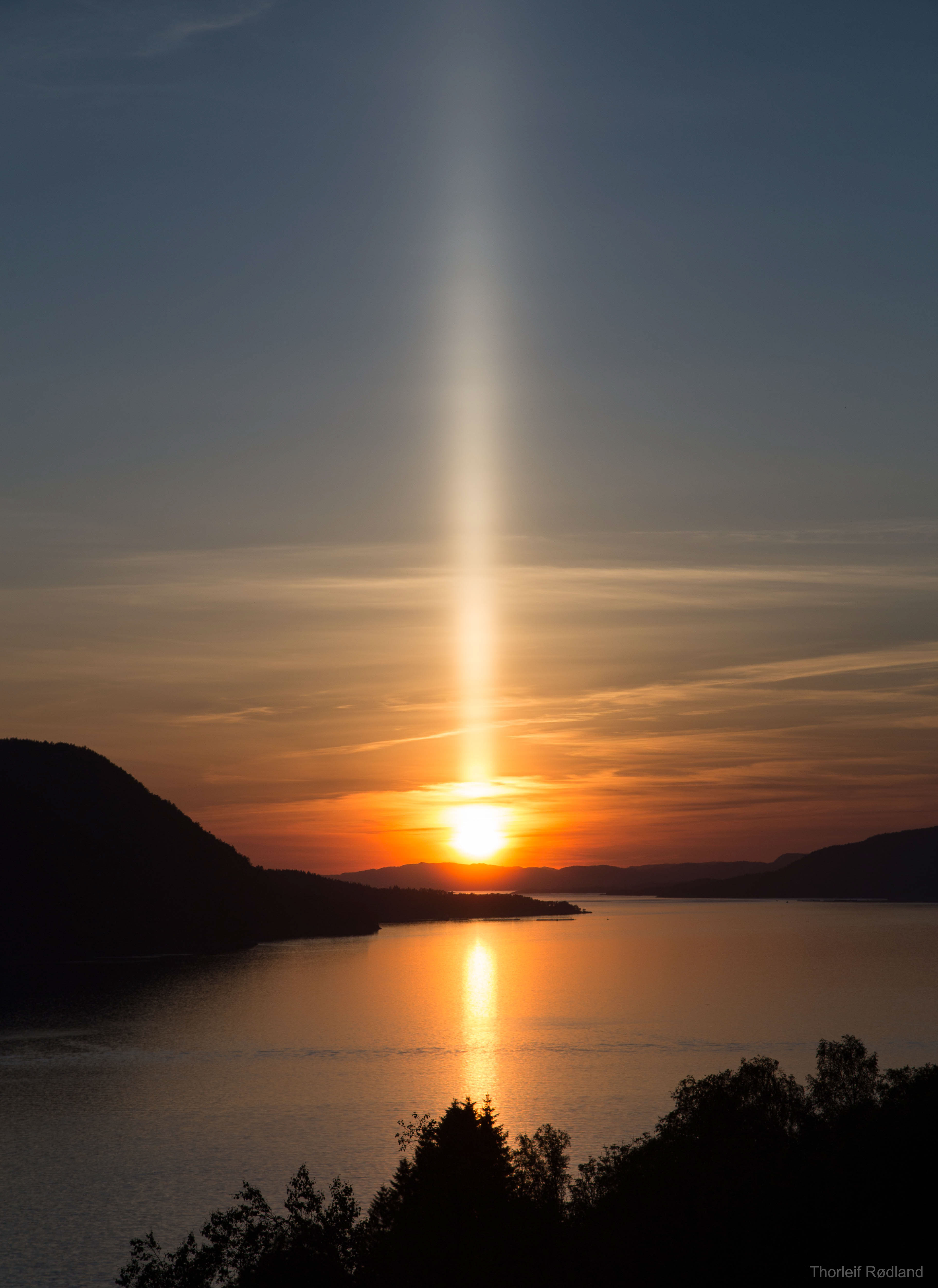 Have you ever seen a sun pillar? When the air is cold and the Sun is rising or setting, falling ice crystals can reflect sunlight and create an unusual column of light. Ice sometimes forms flat, six-sided shaped crystals as it falls from high-level clouds. Air resistance causes these crystals to lie nearly flat much of the time as they flutter to the ground. Sunlight reflects off crystals that are properly aligned, creating the sun-sun-pillar effect. In the featured picture taken last week, a sun-pillar reflects light from a Sun setting over Fensfjorden, Norway.