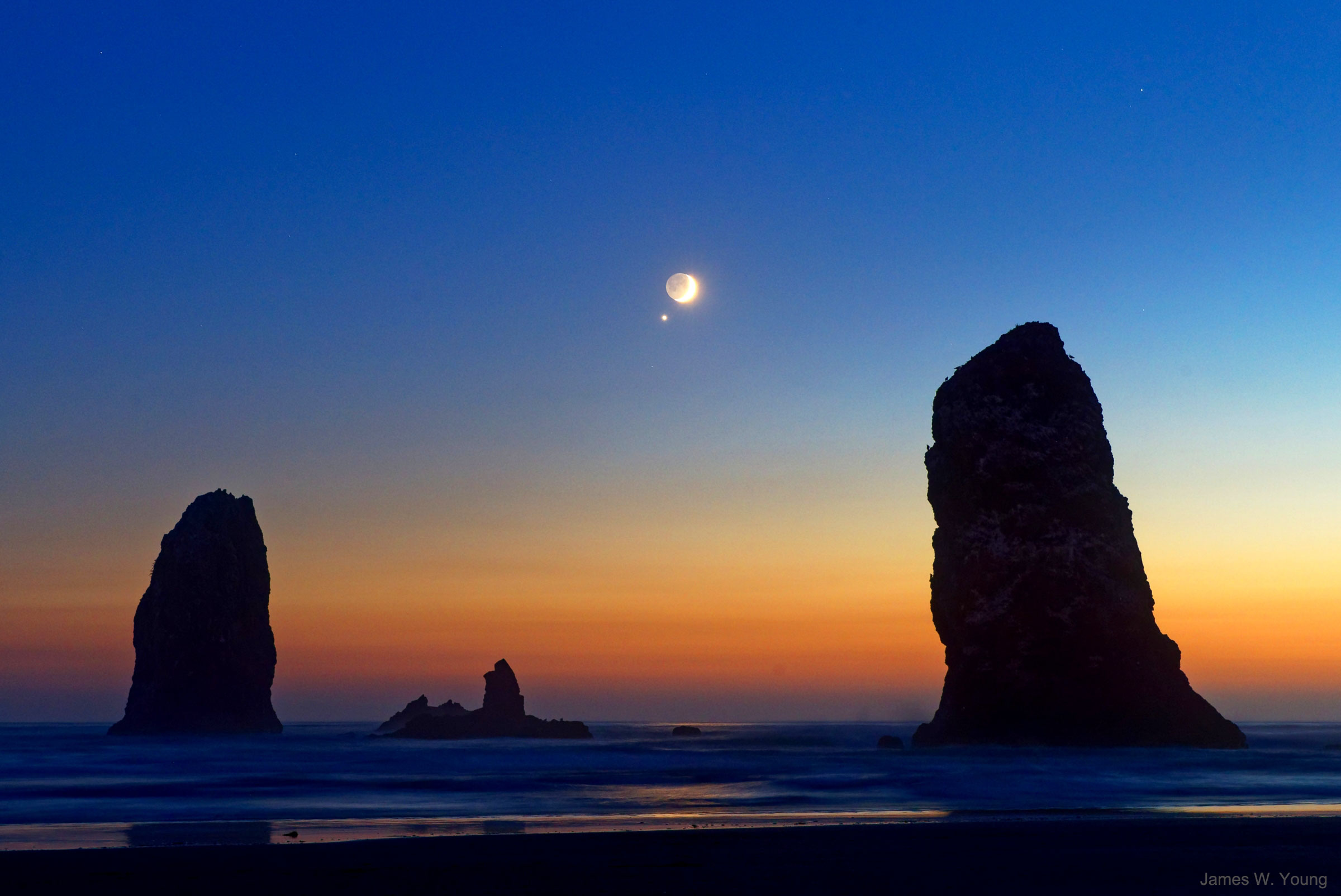 What's that spot next to the Moon? Venus. Two days ago, the crescent Moon slowly drifted past Venus, appearing within just one degree at its closest. This conjunction, though, was just one of several photographic adventures for our Moon this month (moon-th), because, for one, a partial solar eclipse occurred just a few days before, on July 12. Currently, the Moon appears to be brightening, as seen from the Earth, as the fraction of its face illuminated by the Sun continues to increase. In a few days, the Moon will appear more than half full, and therefore be in its gibbous phase. Next week the face of the Moon that always faces the Earth will become, as viewed from the Earth, completely illuminated by the Sun. Even this full phase will bring an adventure, though, as a total eclipse of this Thunder Moon will occur on July 27. Don't worry about our Luna getting tired, though, because she'll be new again next month (moon-th) -- August 11 to be exact -- just as she causes another partial eclipse of the Sun. Pictured, Venus and the Moon were captured from Cannon Beach above a rock formation off the Oregon (USA) coast known as the Needles. About an hour after this image was taken, the spin of the Earth caused both Venus and the Moon to set.