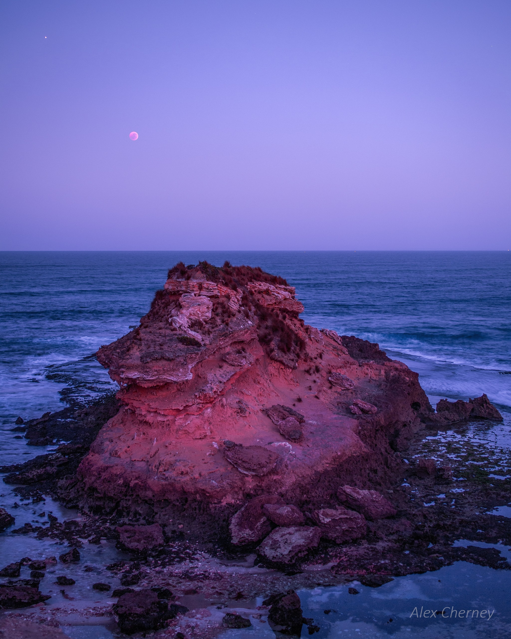 Mars is also known as The Red Planet, often seen with a reddish tinge in dark night skies. Mars shines brightly at the upper left of this gorgeous morning twilight view from Mornington Peninsula, Victoria, Australia, but the Moon and planet Earth look redder still. Taken on July 27, the totally eclipsed Moon is setting. It looks reddened because the Earth's umbral shadow isn't completely dark. Instead Earth's shadow is suffused with a faint red light from all the planet's sunsets and sunrises seen from the perspective of an eclipsed Moon. The sunsets and sunrises are reddened because Earth's atmosphere scatters blue light more strongly than red, creating the faint bluish twilight sky. Of course, craggy seaside rocks also take on the reddened colors of this Australian sunrise.