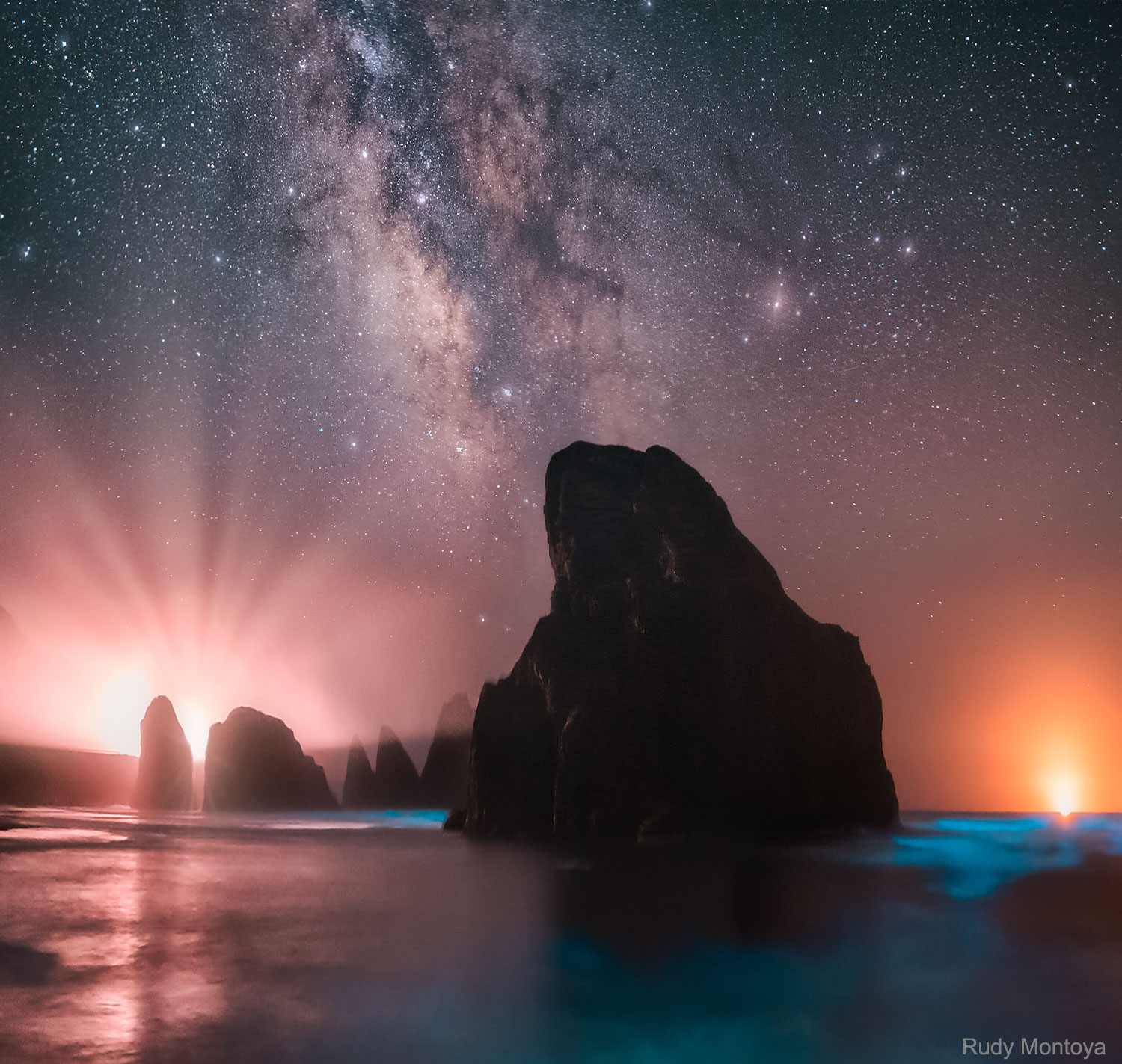 very step caused the sand to light up blue. That glow was bioluminescence -- a blue radiance that also lights the surf in this surreal scene captured last month at Meyer's Creek Beach in Oregon, USA. Volcanic stacks dot the foreground sea, while a thin fog layer scatters light on the horizon. The rays of light spreading from the left horizon were created by car headlights on the Oregon Coast Highway (US 101), while the orange light on the right horizon emanates from a fishing boat. Visible far in the distance is the band of our Milky Way Galaxy, appearing to rise from a dark rocky outcrop. Sixteen images were added together to bring up the background Milky Way and to reduce noise. Follow APOD on: Facebook, Google Plus, Instagram, or Twitter
