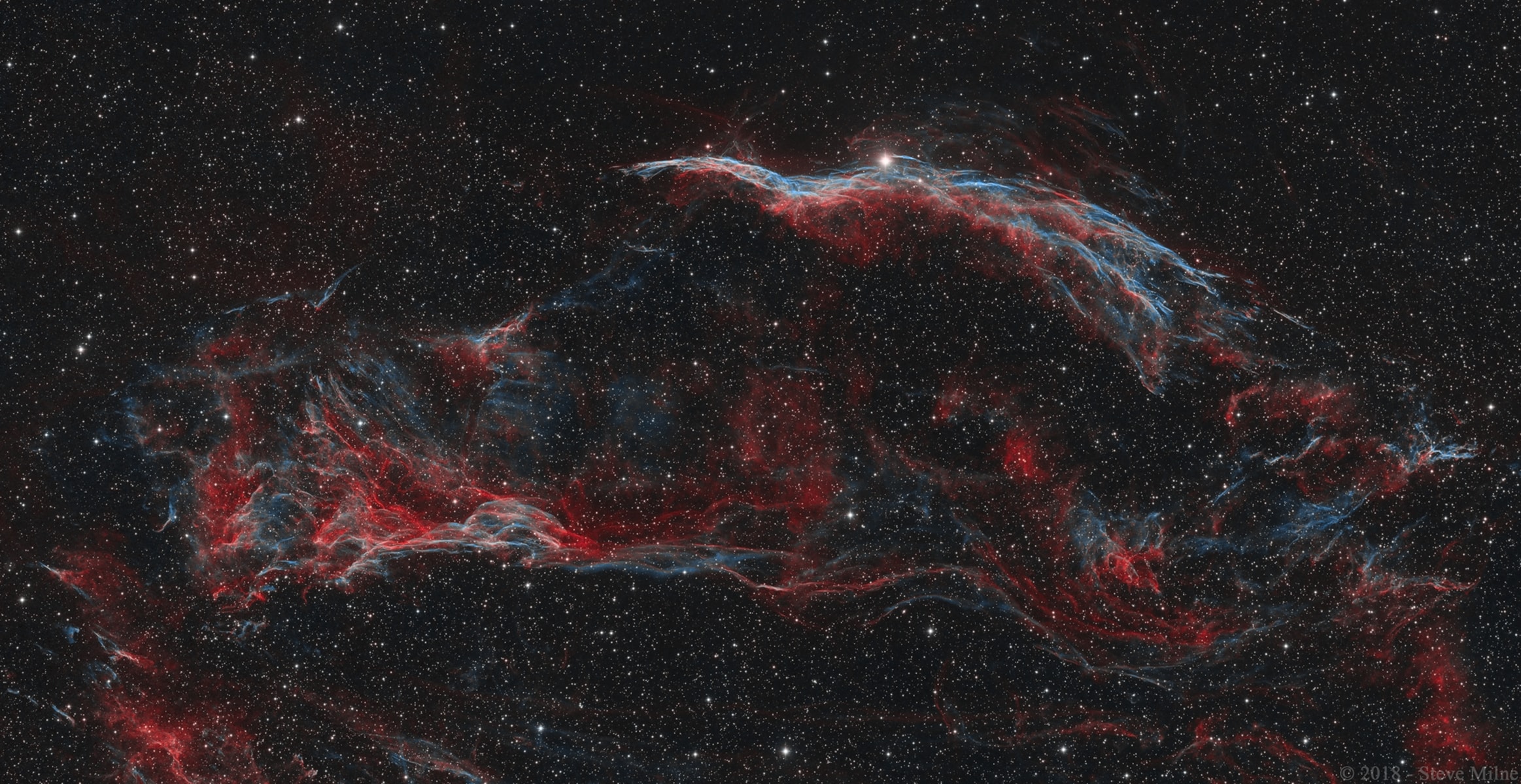 Delicate in appearance, these filaments of shocked, glowing gas, are draped across planet Earth's sky toward the constellation of Cygnus. They form the western part of the Veil Nebula. The Veil Nebula itself is a large supernova remnant, an expanding cloud born of the death explosion of a massive star. Light from the original supernova explosion likely reached Earth over 5,000 years ago. Blasted out in the cataclysmic event, the interstellar shock wave plows through space sweeping up and exciting interstellar material. The glowing filaments are really more like long ripples in a sheet seen almost edge on, remarkably well separated into atomic hydrogen (red) and oxygen (blue-green) gas. Also known as the Cygnus Loop, the Veil Nebula now spans nearly 3 degrees or about 6 times the diameter of the full Moon. While that translates to over 70 light-years at its estimated distance of 1,500 light-years, this telescopic two panel mosaic image of the western portion spans about half that distance. Brighter parts of the western Veil are recognized as separate nebulae, including The Witch's Broom (NGC 6960) along the top of this view and Pickering's Triangle (NGC 6979) below and left.