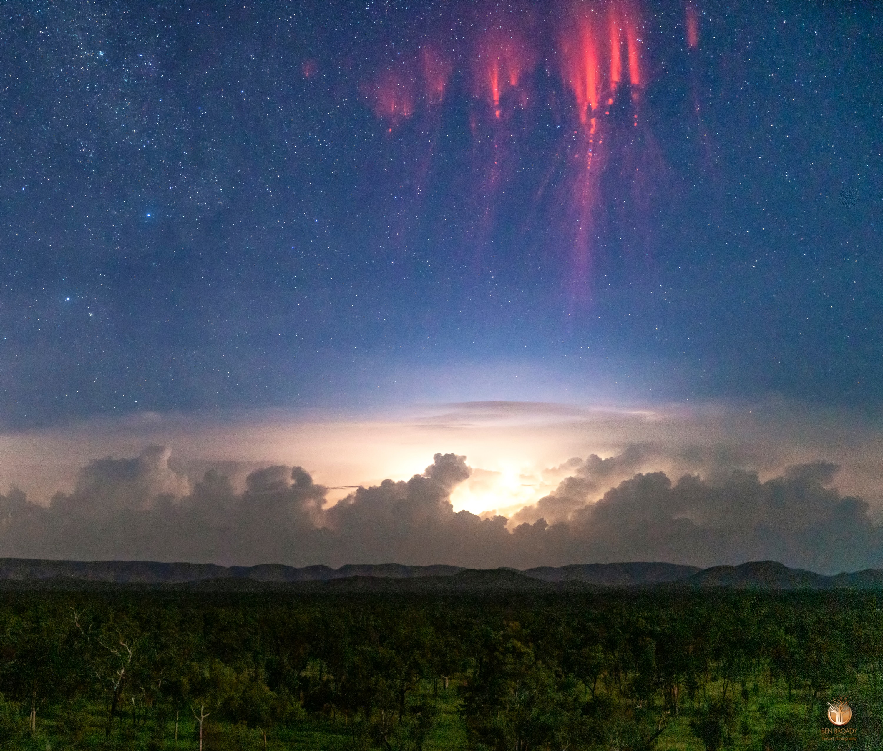 What are those red filaments in the sky? It is a rarely seen form of lightning confirmed only about 30 years ago: red sprites. Recent research has shown that following a powerful positive cloud-to-ground lightning strike, red sprites may start as 100-meter balls of ionized air that shoot down from about 80-km high at 10 percent the speed of light and are quickly followed by a group of upward streaking ionized balls. The featured image, taken just over a week ago in Kununurra, Western Australia, captured some red sprites while shooting a time-lapse sequence of a distant lightning storm. Pictured, green trees cover the foreground, dark mountains are seen on the horizon, ominous storm clouds hover over the distant land, while red sprites appear in front of stars far in the distance. Red sprites take only a fraction of a second to occur and are best seen when powerful thunderstorms are visible from the side.