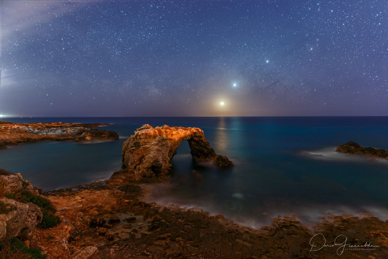 This was a sunrise to remember. About a month ago, just before the dawn of the Sun, an impressive alignment of celestial objects was on display to the east. Pictured, brightest and closest to the horizon, is the Moon. The Moon's orange glow is caused by the scattering away of blue light by the intervening atmosphere. Next brightest and next closest to the horizon is the planet Venus. Compared to the Moon, Venus appears more blue -- as can (also) be seen in its reflection from the water. Next up is Jupiter, while the bright object above Jupiter is the star Antares. Although this display was visible from almost anywhere on planet Earth, the featured image was taken along a picturesque seashore near the city of Syracuse, on the island of Sicily, in the country of Italy. This month Saturn appears between Venus and Jupiter before sunrise, while Mars is visible just after sunset.