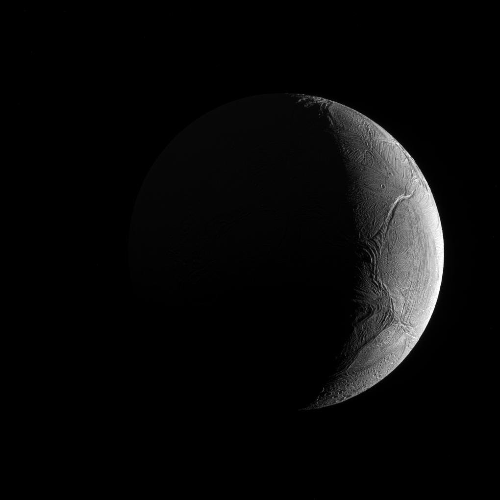 Peering from the shadows, the Saturn-facing hemisphere of tantalizing inner moon Enceladus poses in this Cassini spacecraft image. North is up in the dramatic scene captured during November 2016 as Cassini's camera was pointed in a nearly sunward direction about 130,000 kilometers from the moon's bright crescent. In fact, the distant world reflects over 90 percent of the sunlight it receives, giving its surface about the same reflectivity as fresh snow. A mere 500 kilometers in diameter, Enceladus is a surprisingly active moon. Data collected during Cassini's flybys and years of images have revealed the presence of remarkable south polar geysers and a possible global ocean of liquid water beneath an icy crust.