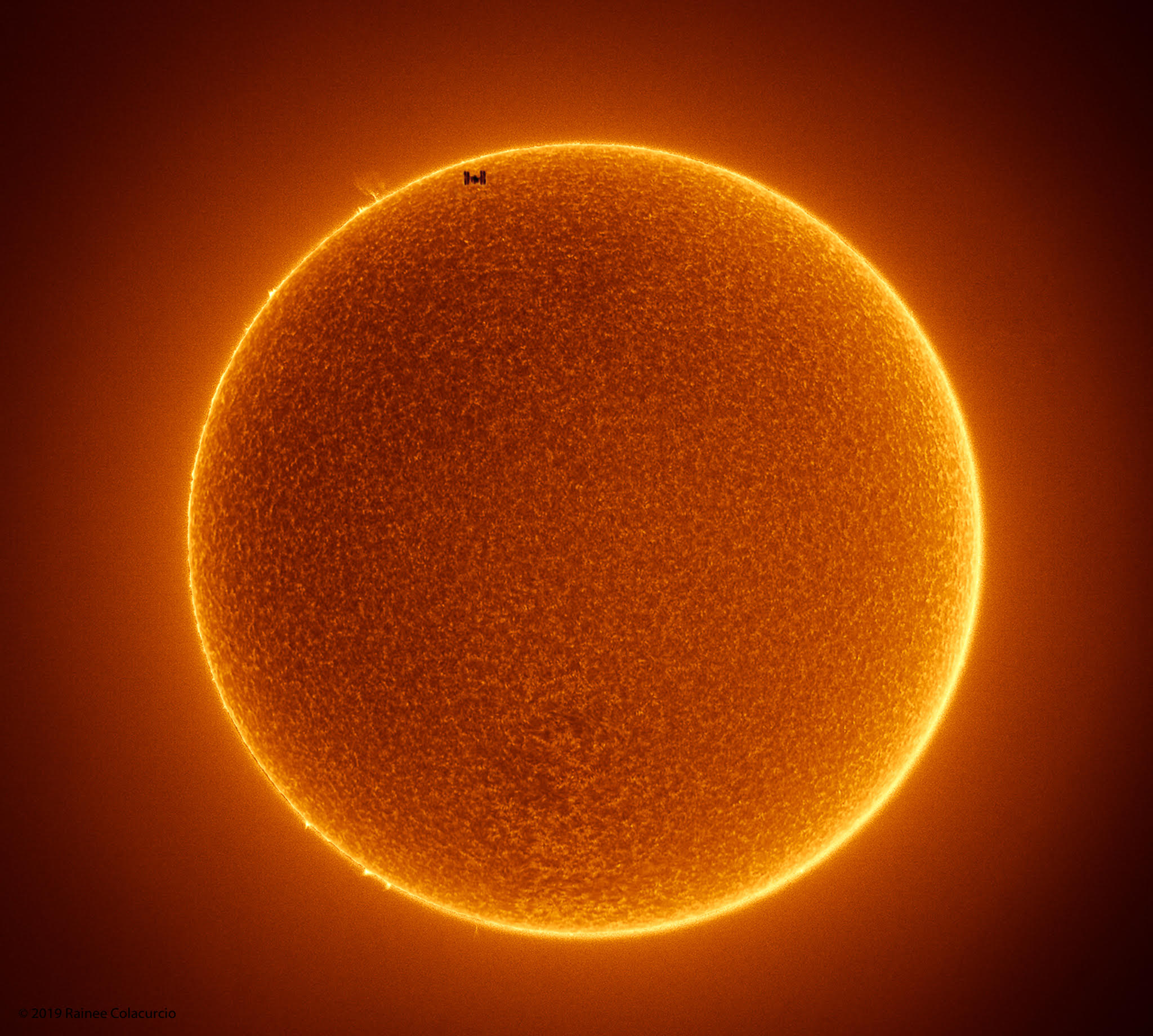 That's no sunspot. It's the International Space Station (ISS) caught passing in front of the Sun. Sunspots, individually, have a dark central umbra, a lighter surrounding penumbra, and no solar panels. By contrast, the ISS is a complex and multi-spired mechanism, one of the largest and most sophisticated machines ever created by humanity. Also, sunspots occur on the Sun, whereas the ISS orbits the Earth. Transiting the Sun is not very unusual for the ISS, which orbits the Earth about every 90 minutes, but getting one's timing and equipment just right for a great image is rare. Strangely, besides that fake spot, in this recent two-image composite, the Sun lacked any real sunspots. The featured picture combines two images -- one capturing the space station transiting the Sun -- and another taken consecutively capturing details of the Sun's surface. Sunspots have been rare on the Sun since the dawn of the current Solar Minimum, a period of low solar activity. For reasons not yet fully understood, the number of sunspots occurring during both the previous and current solar minima have been unusually low.