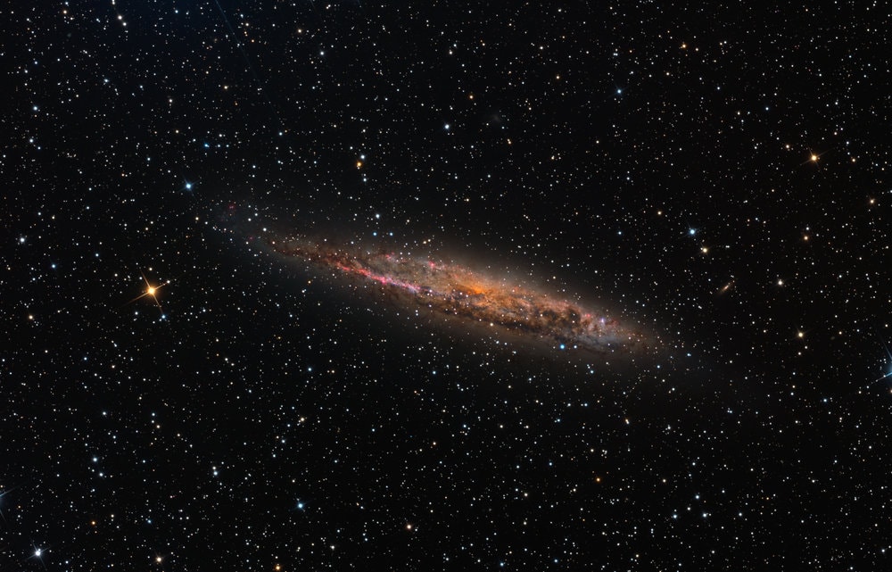 Large spiral galaxy NGC 4945 is seen edge-on near the center of this cosmic galaxy portrait. In fact, it's almost the size of our Milky Way Galaxy. NGC 4945's own dusty disk, young blue star clusters, and pink star forming regions standout in the sharp, colorful telescopic image. About 13 million light-years distant toward the expansive southern constellation Centaurus, NGC 4945 is only about six times farther away than Andromeda, the nearest large spiral galaxy to the Milky Way. Though this galaxy's central region is largely hidden from view for optical telescopes, X-ray and infrared observations indicate significant high energy emission and star formation in the core of NGC 4945. Its obscured but active nucleus qualifies the gorgeous island universe as a Seyfert galaxy and home to a central supermassive black hole.