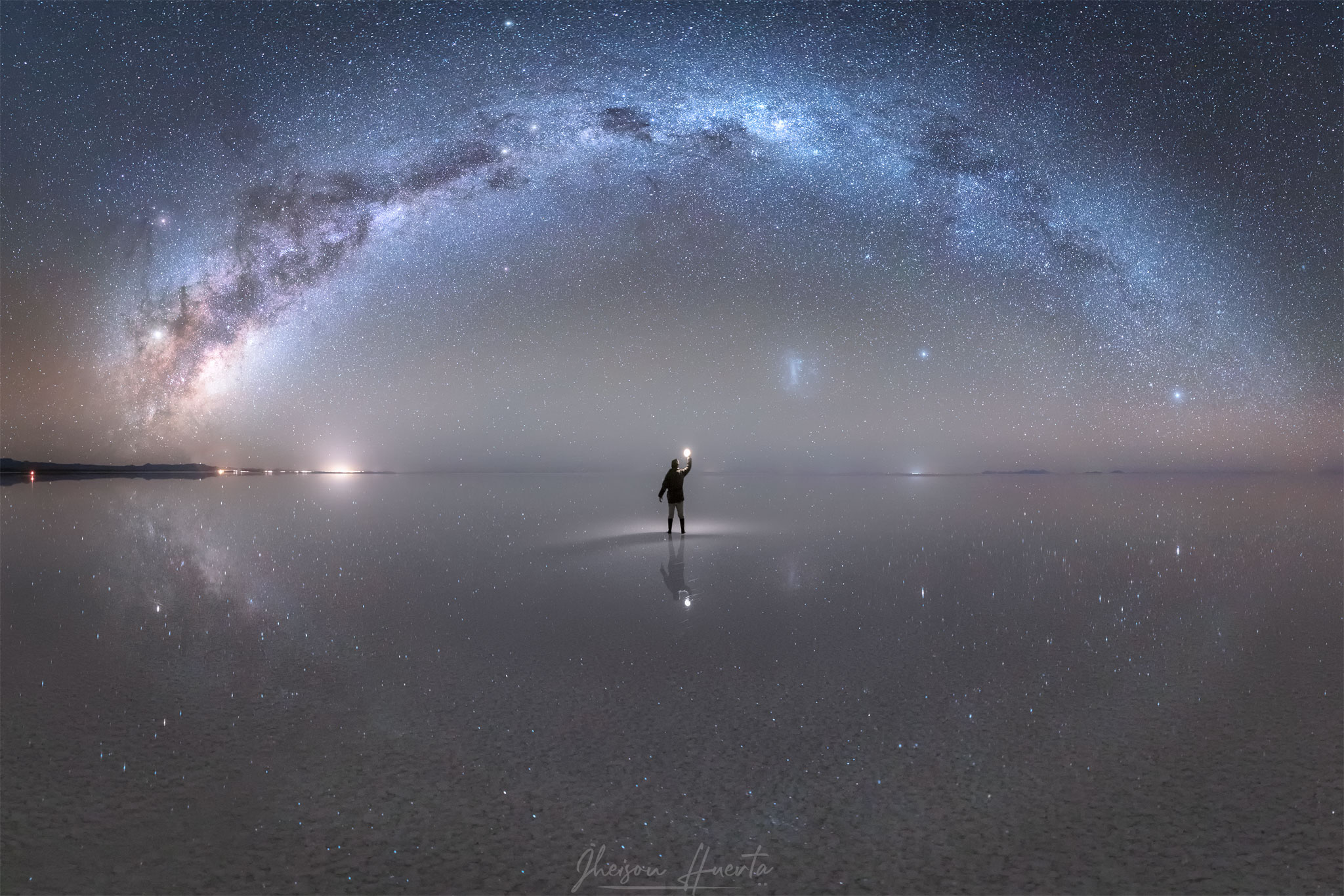 What's being reflected in the world's largest mirror? Stars, galaxies, and a planet. Many of these stars are confined to the grand arch that runs across the image, an arch that is the central plane of our home Milky Way Galaxy. Inside the arch is another galaxy -- the neighboring Large Magellanic Cloud (LMC). Stars that are individually visible include Antares on the far left and Sirius on the far right. The planet Jupiter shines brightly just below Antares. The featured picture is composed of 15 vertical frames taken consecutively over ten minutes from the Uyuni Salt Flat in Bolivia. Uyuni Salt Flat (Salar de Uyuni) is the largest salt flat on Earth and is so large and so extraordinarily flat that, after a rain, it can become the world's largest mirror -- spanning 130 kilometers. This expansive mirror was captured in early April reflecting each of the galaxies, stars, and planet mentioned above.