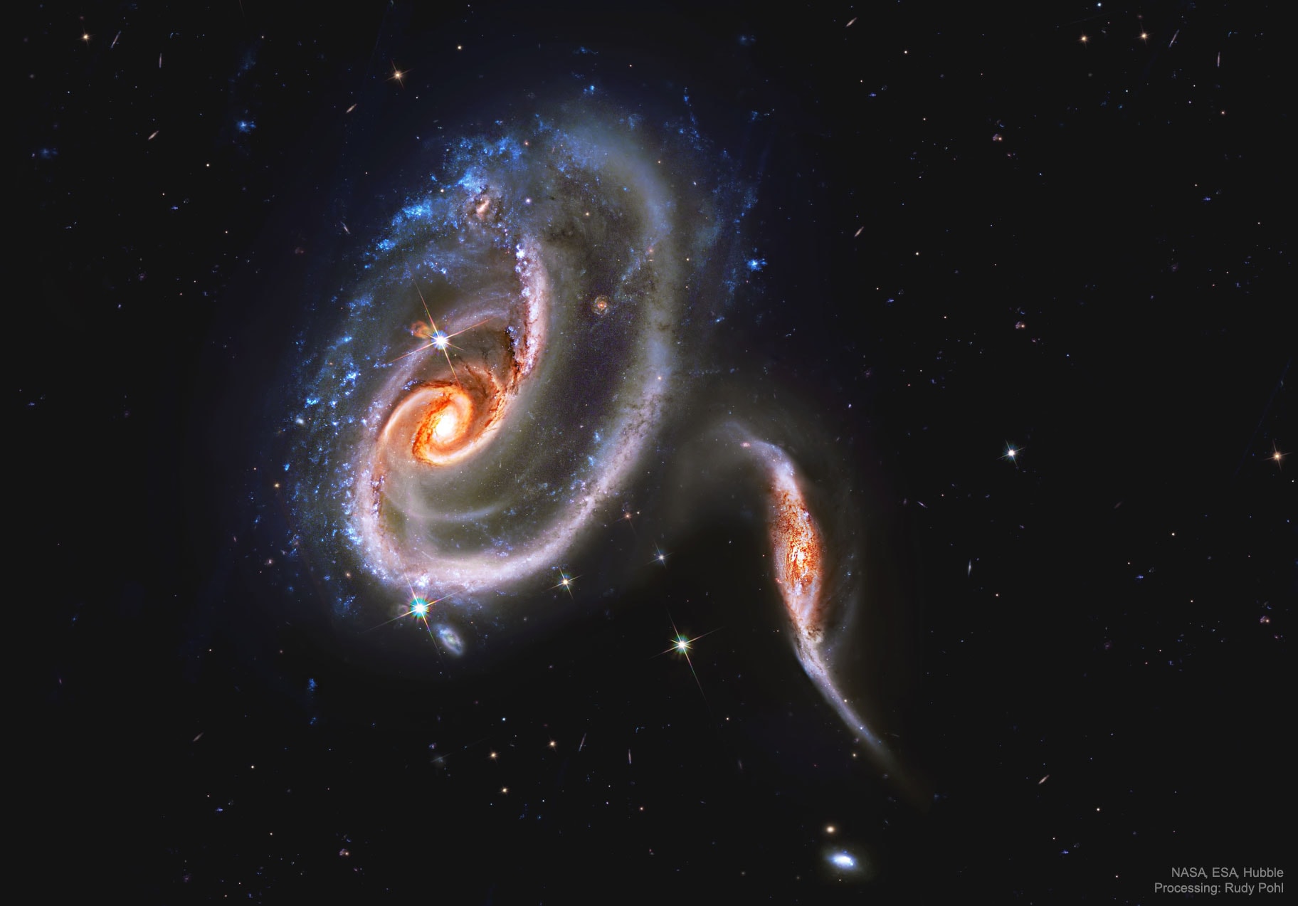 What's happening to these spiral galaxies? Although details remain uncertain, there sure seems to be a titanic battle going on. The upper galaxy is labelled UGC 1810 by itself, but together with its collisional partners is known as Arp 273. The overall shape of the UGC 1810 -- in particular its blue outer ring -- is likely a result of wild and violent gravitational interactions. The blue color of the outer ring at the top is caused by massive stars that are blue hot and have formed only in the past few million years. The inner part of the upper galaxy -- itself an older spiral galaxy -- appears redder and threaded with cool filamentary dust. A few bright stars appear well in the foreground, unrelated to colliding galaxies, while several far-distant galaxies are visible in the background. Arp 273 lies about 300 million light years away toward the constellation of Andromeda. Quite likely, UGC 1810 will devour its galactic sidekicks over the next billion years and settle into a classic spiral form.