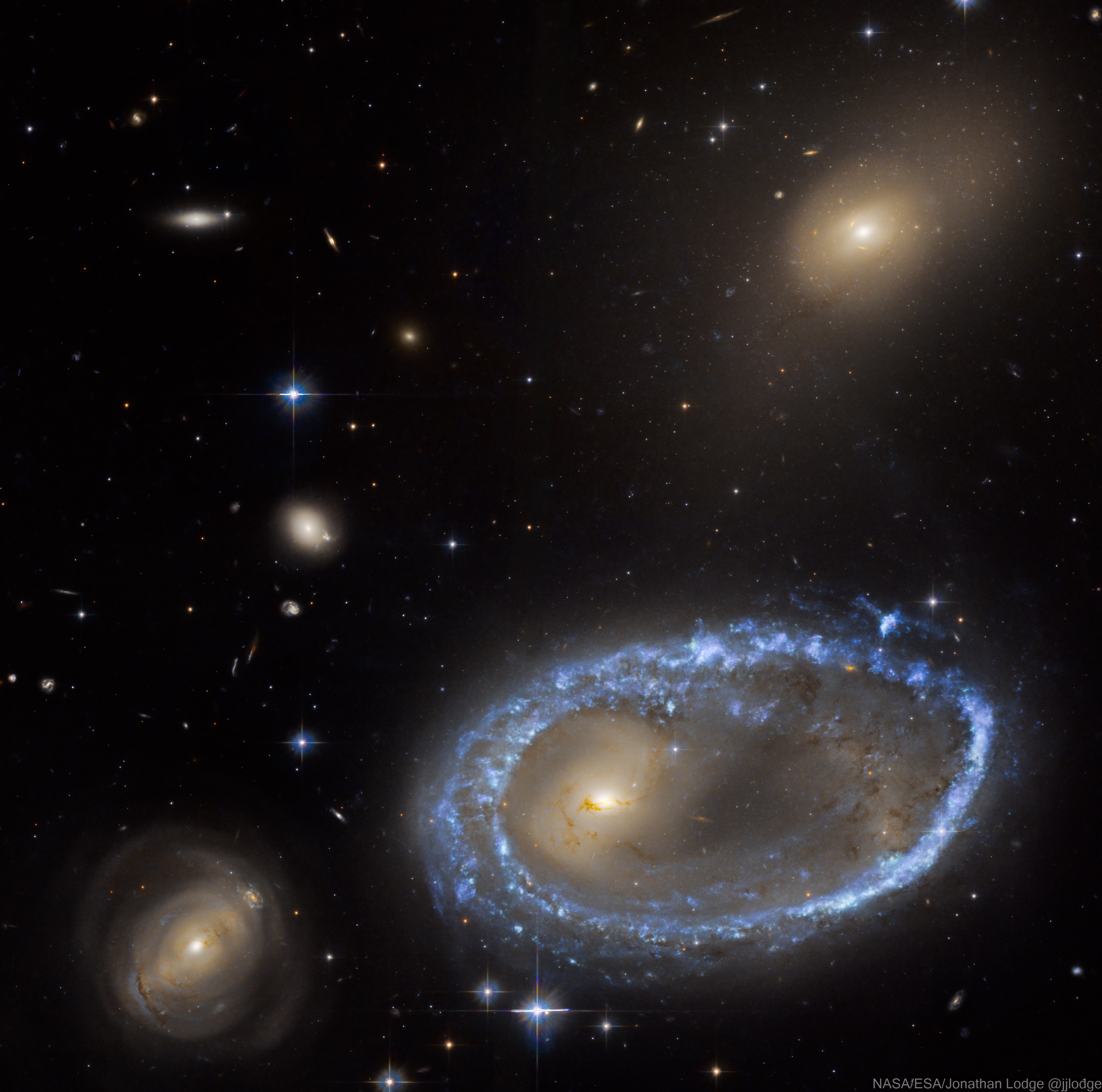 The rim of the large blue galaxy at the right is an immense ring-like structure 150,000 light years in diameter composed of newly formed, extremely bright, massive stars. AM 0644-741 is known as a ring galaxy and was caused by an immense galaxy collision. When galaxies collide, they pass through each other and their individual stars rarely come into contact. The large galaxy's ring-like shape is the result of the gravitational disruption caused by a small intruder galaxy passing through it. When this happens, interstellar gas and dust become compressed, causing a wave of star formation to move out from the impact point like a ripple across the surface of a pond. Other galaxies in the field of view are background galaxies, not interacting with AM 0644-741. Foreground spiky stars are within our own Milky Way. But the smaller intruder galaxy is caught above and right, near the top of the frame taken by the Hubble Space Telescope. Ring galaxy AM 0644-741 lies about 300 million light years away toward the southern constellation Volans.