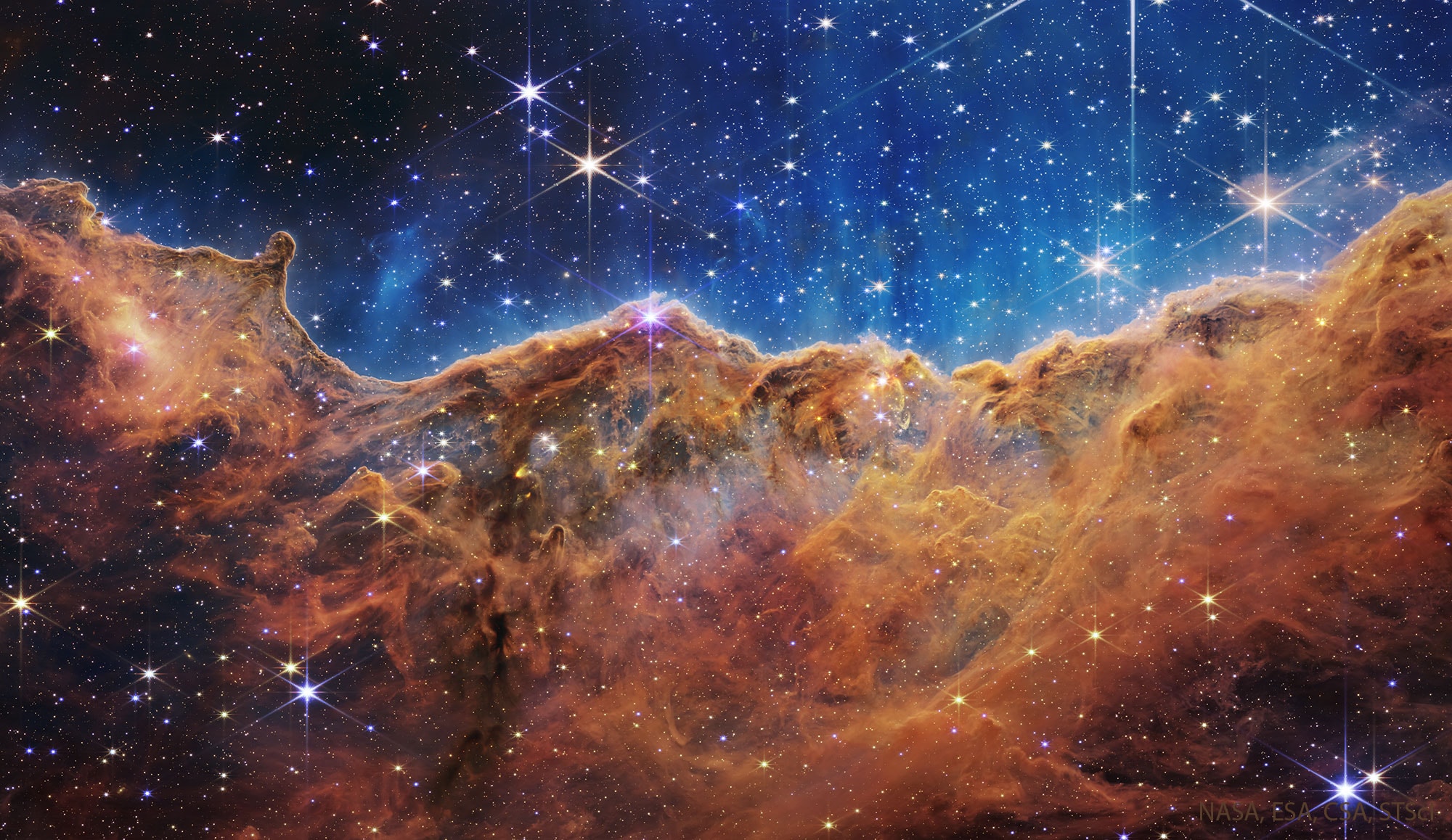 Stars created these cliffs. Specifically, the destructive winds and energetic light from the stars in the open cluster NGC 3324 eroded away part of a mountain of dark interstellar dust in the northern part of the Carina Nebula. Several of these stars are visible toward the top of this highly detailed image taken recently by the James Webb Space Telescope, the largest astronomical telescope ever launched. Webb's large mirror and ability to see dust-piercing infrared light has enabled it to capture fascinating details in the dust, hundreds of previously hidden stars, and even some galaxies far in the distance. The featured jagged cliffs occur in part of Carina known as the Gabriela Mistral Nebula -- because when viewed in another orientation, they appear similar to the facial profile of the famous Chilean poet. These nebular cliffs occur about 7,600 light years away toward the southern constellation of Carina. Astrophysicists: Browse 2,800+ codes in the Astrophysics Source Code Library