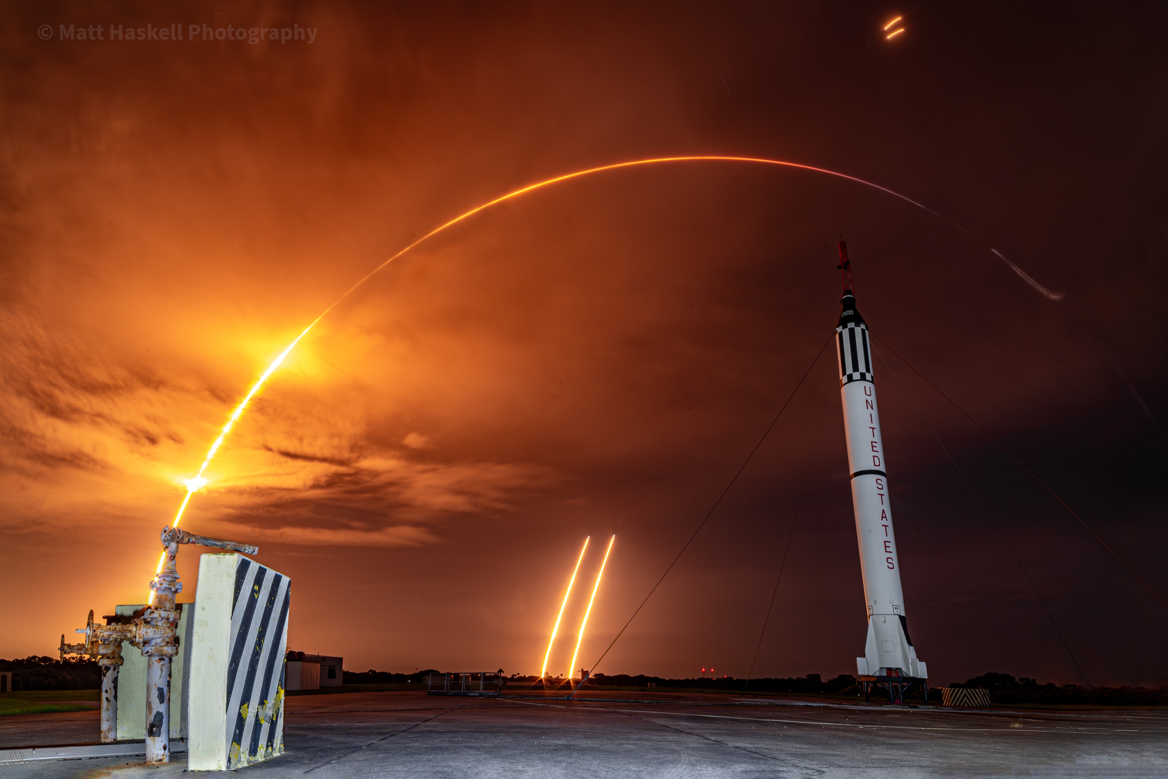 In a photo from the early hours of July 29 (UTC), a Redstone rocket and Mercury capsule are on display at Cape Canaveral Launch Complex 5. Beyond the Redstone, the 8 minute long exposure has captured the arcing launch streak of a SpaceX Falcon Heavy rocket. The Falcon's heavy communications satellite payload, at a record setting 9 metric tons, is bound for geosynchronous orbit some 22,000 miles above planet Earth. The historic launch of a Redstone rocket carried astronaut Alan Shepard on a suborbital spaceflight in May 1961 to an altitude of about 116 miles. Near the top of the frame, this Falcon rocket's two reusable side boosters separate and execute brief entry burns. They returned to land side by side at Canaveral's Landing Zone 1 and 2 in the distance.