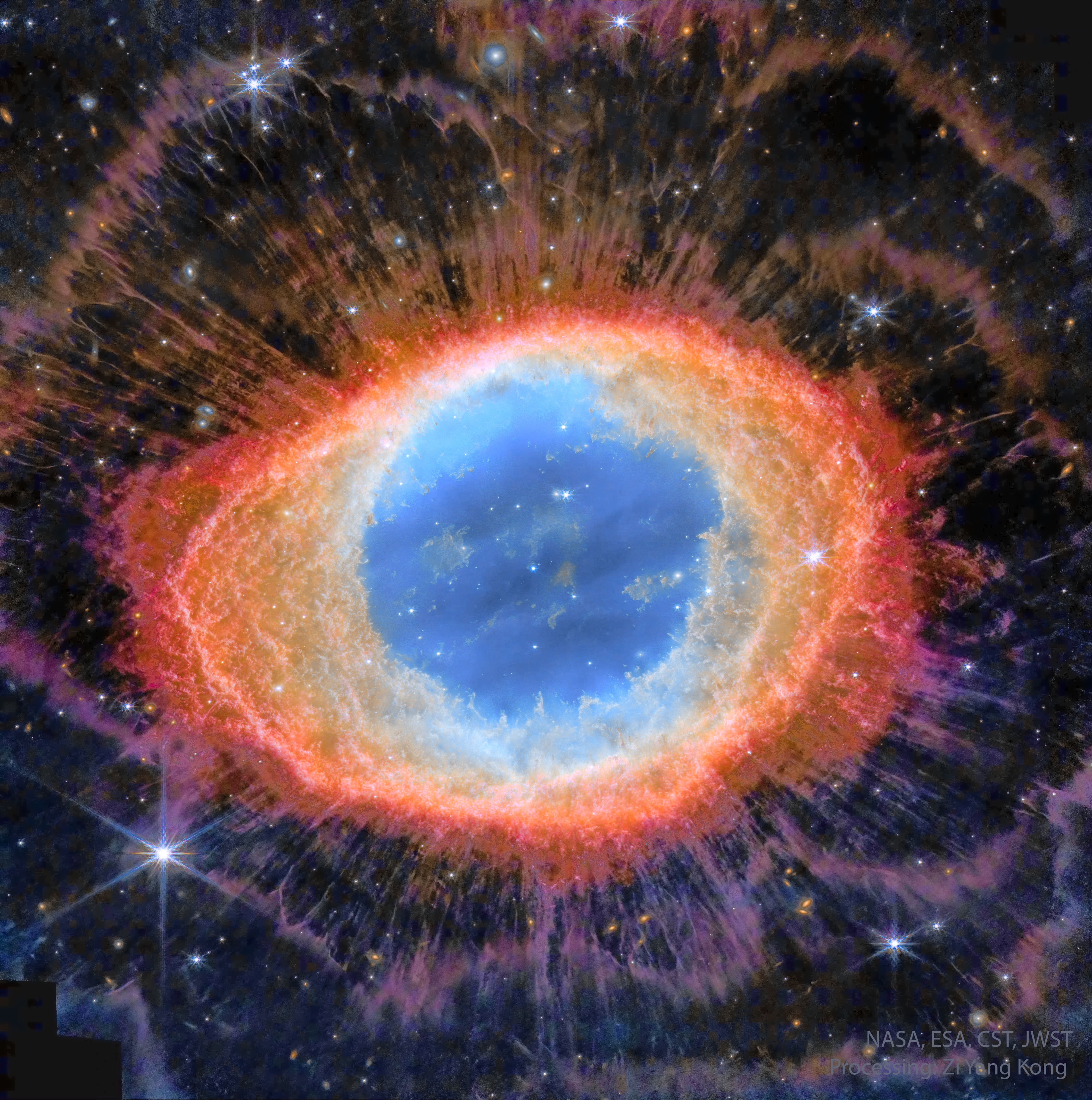 The Ring Nebula (M57), is more complicated than it appears through a small telescope. The easily visible central ring is about one light-year across, but this remarkable exposure by the James Webb Space Telescope explores this popular nebula with a deep exposure in infrared light. Strings of gas, like eyelashes around a cosmic eye, become evident around the Ring in this digitally enhanced featured image in assigned colors. These long filaments may be caused by shadowing of knots of dense gas in the ring from energetic light emitted within. The Ring Nebula is an elongated planetary nebula, a type of gas cloud created when a Sun-like star evolves to throw off its outer atmosphere to become a white dwarf star. The central oval in the Ring Nebula lies about 2,500 light-years away toward the musical constellation Lyra.