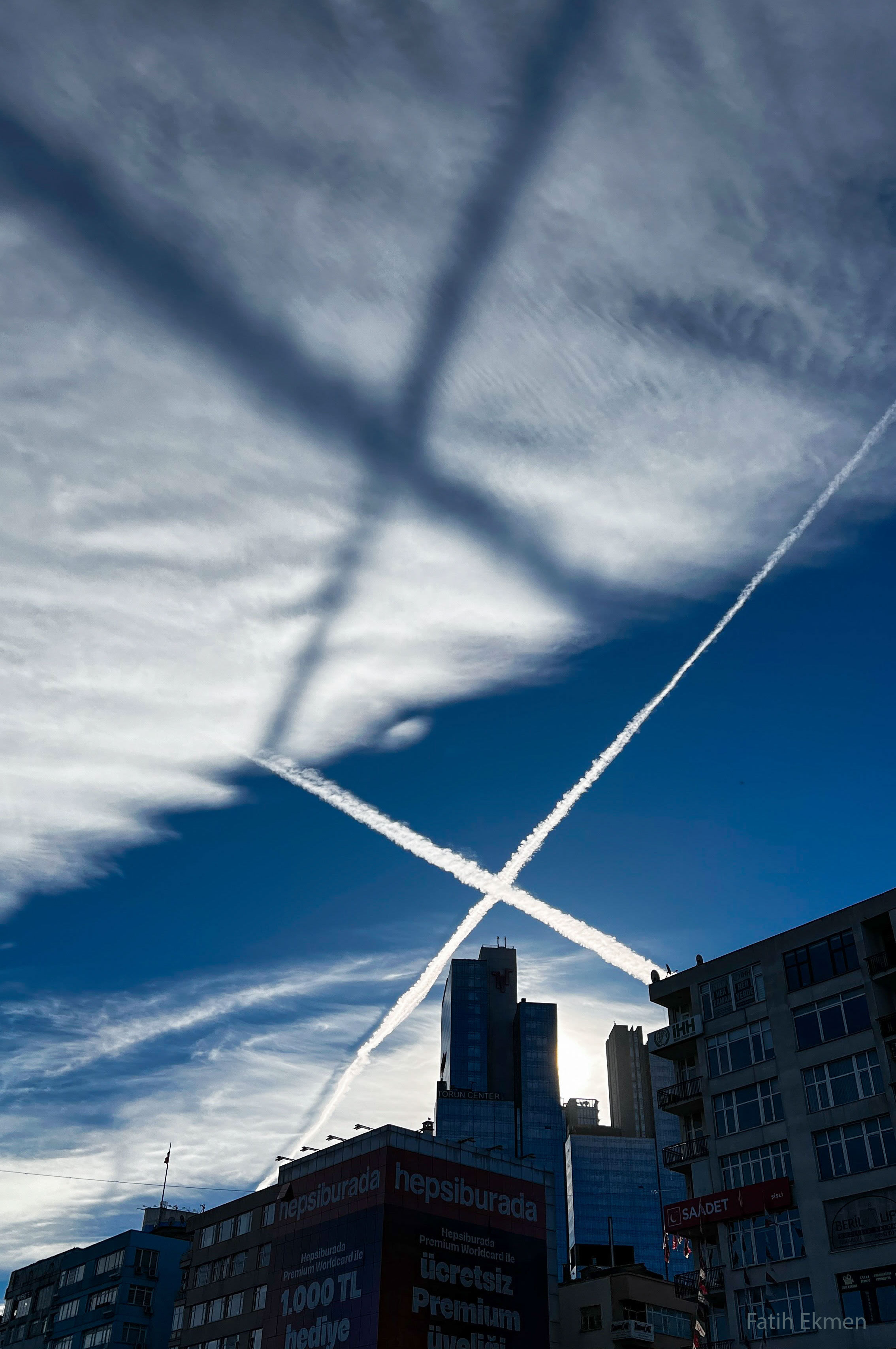 What created this giant X in the clouds? It was the shadow of contrails. When airplanes fly, humid engine exhaust may form water droplets that might freeze in Earth's cold upper atmosphere. These persistent streams of water and ice scatter light from the Sun above and so appear bright. These contrails cast long shadows. That was just the case over Istanbul, Türkiye, earlier this month. Contrails occur all over planet Earth and, generally, warm the Earth when the trap infrared light but cool the Earth when they efficiently reflect sunlight. The image was taken by a surprised photographer in the morning on the way to work.