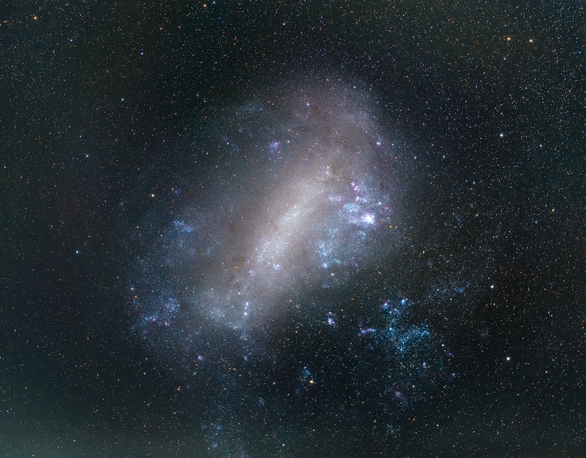 Have you ever seen another galaxy with your own eyes? The featured image shows the Large Magellanic Cloud (LMC), one of the closest neighbors of our Milky Way. If you are anywhere south of latitude 20° N (but the further south, the better), you can see it with the unaided eye if you go to a dark sky location, away from big cities and light polution. It is a dwarf irregular galaxy about 163,000 light-years away, and a member of our Local Group of galaxies. Despite being small, with a total mass approximately equivalent to 10% - 20% of the mass of the Milky Way, the LMC is very actively forming stars. This is likely due in part to the gravitational push and pull of tides caused by the Milky Way on the LMC. Some astronomers have predicted that it will collide with the Milky Way in in about 2 billion years.